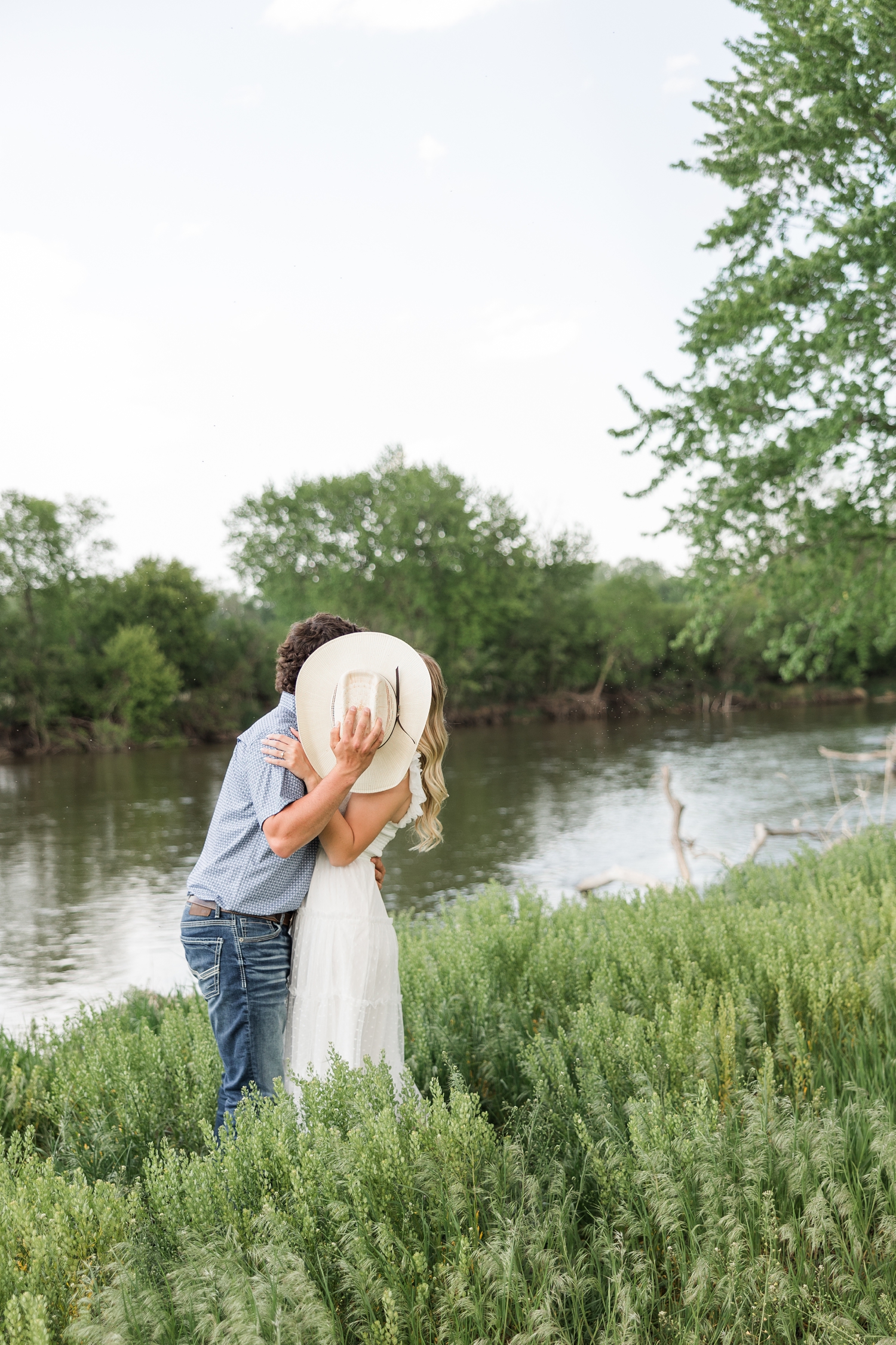 Dawson leans Jade back for a kiss but covers their faces with his cowboy hat with the river as a backdrop | CB Studio