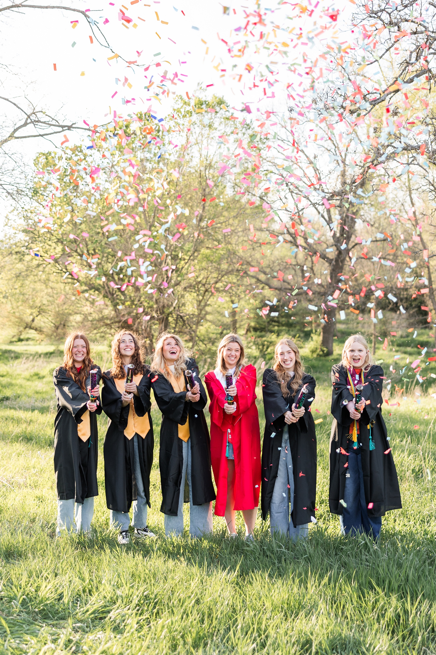 TEAM 26 senior spokesmodels stand in a grassy pasture in their graduation gowns while popping confetti poppers | CB Studio
