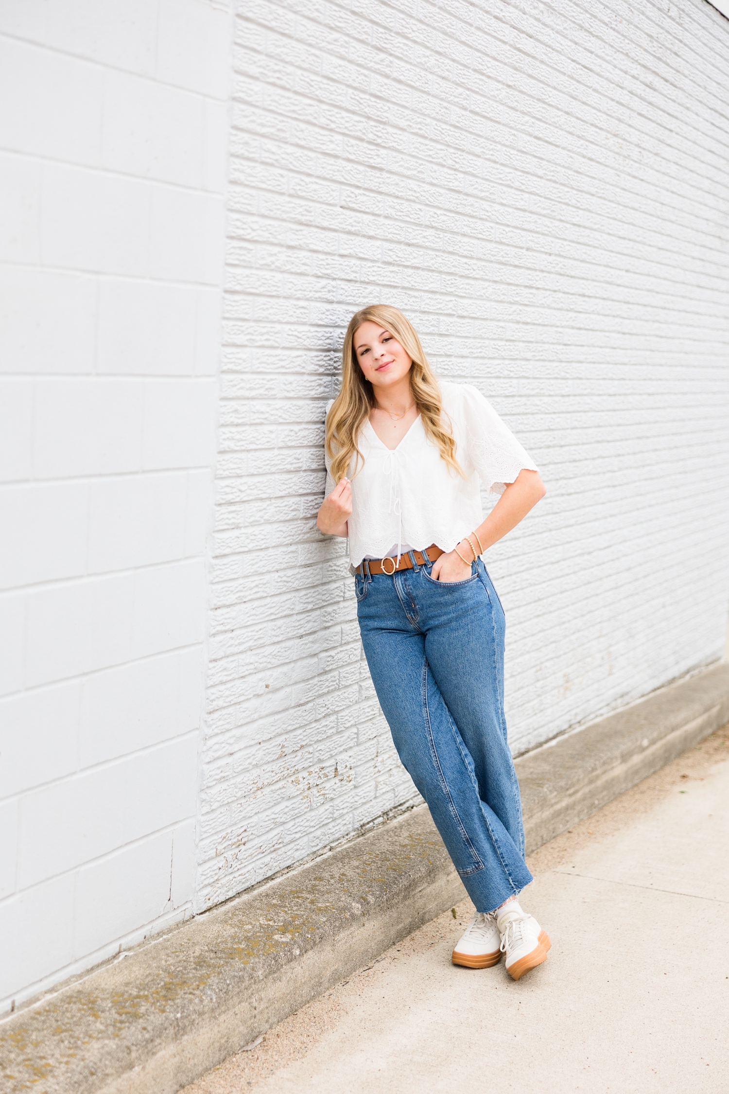 Malea dressed in denim styles, lean against a light blue brick building in Algona, IA | CB Studio