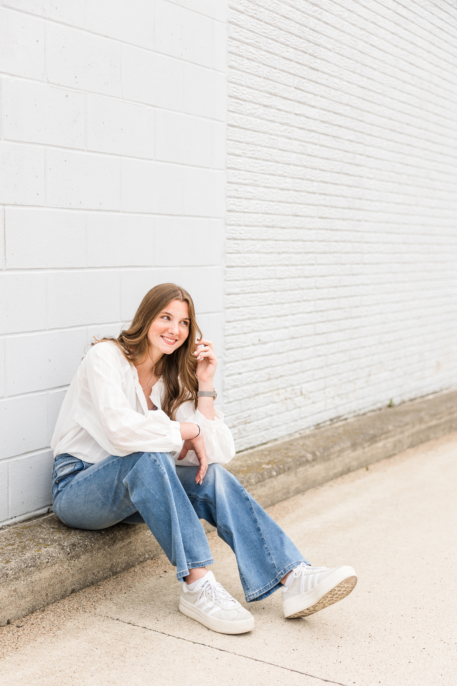 Mya dressed in a denim style, sits along a curb against a light blue brick building in Algona, IA | CB Studio