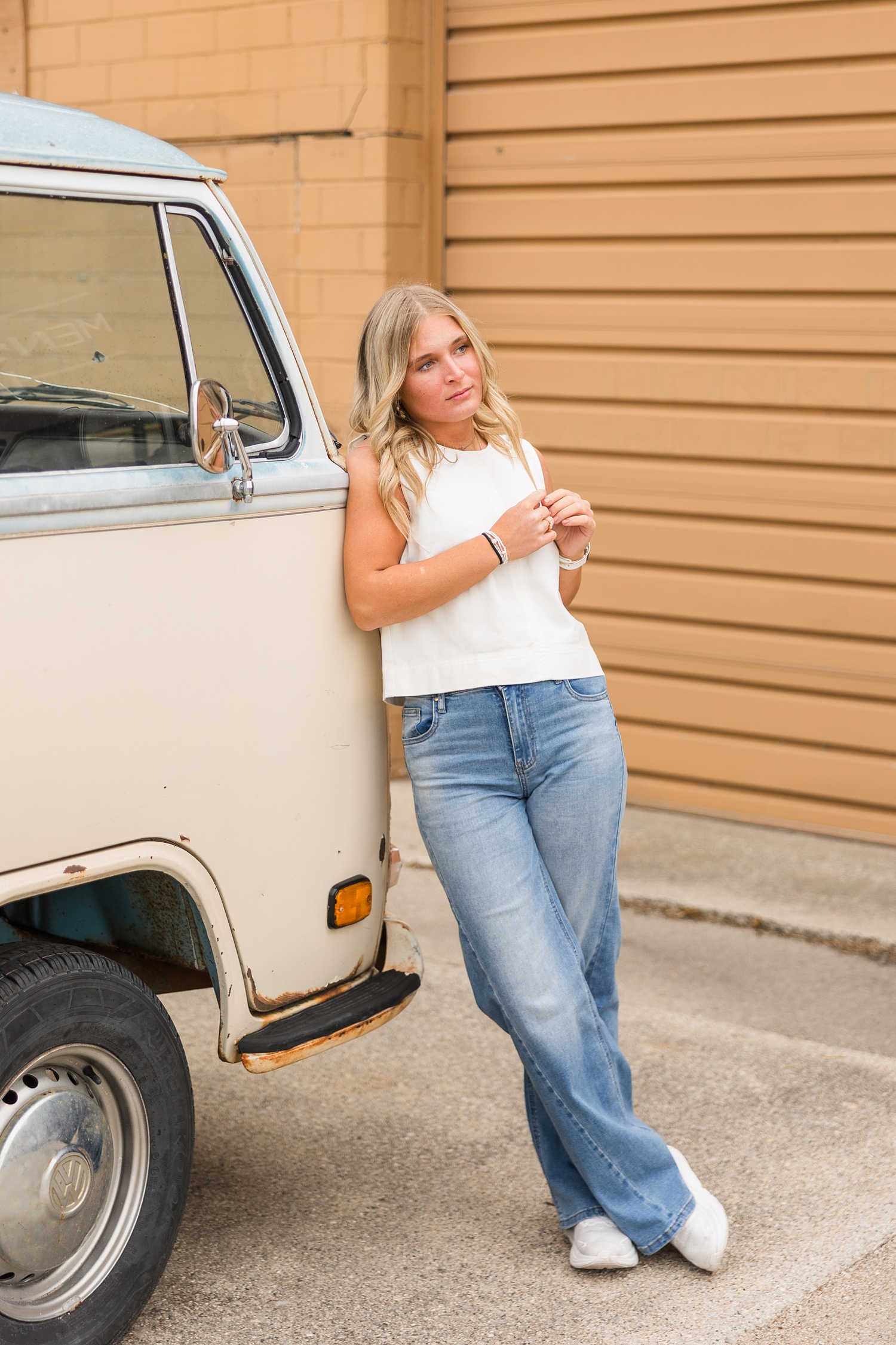 Audrey dressed denim styles, leans against a two-toned tan and light blue Volkswagon van in Algona, IA while pinching her hair and looking off to the right | CB Studio