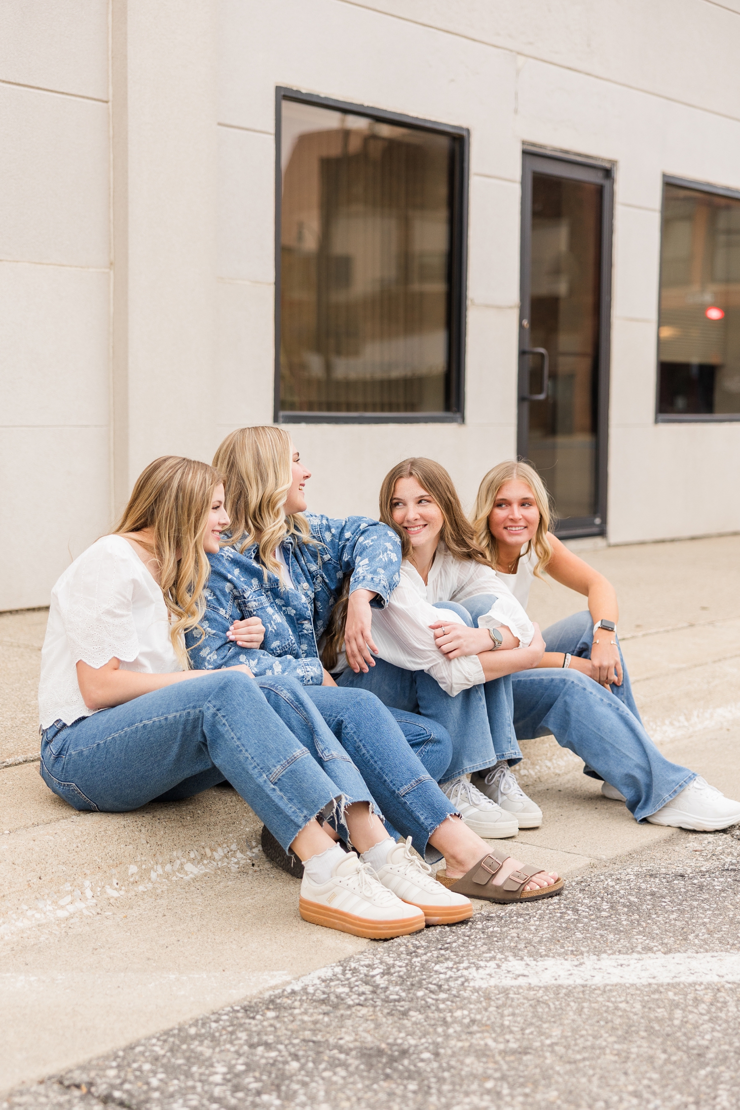 TEAM 27 dressed denim styles, sit along a curb while laughing with each other in downtown Algona, IA | CB Studio