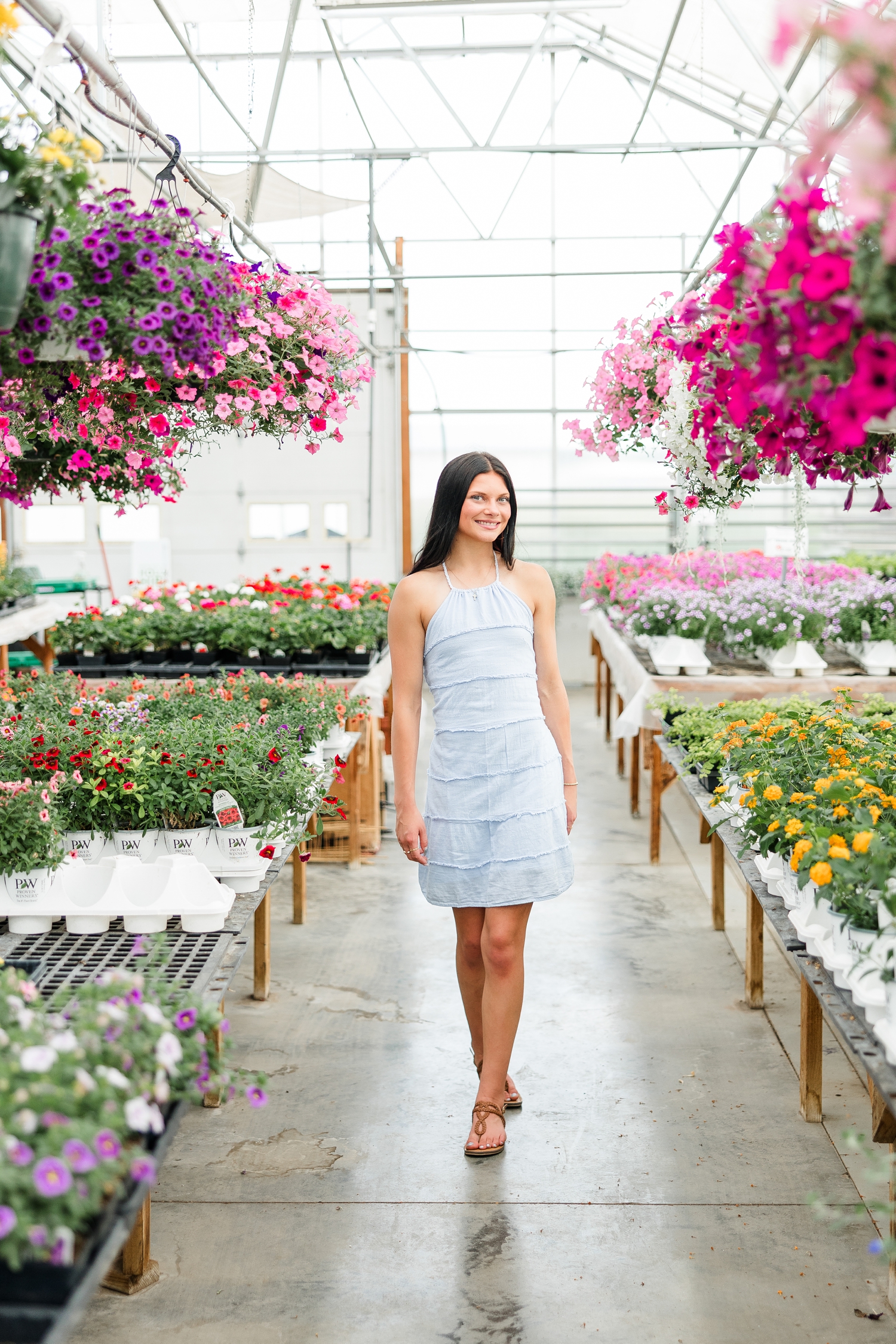 Brooke, wearing a light blue linen dress, smiles as she walks down a floral aisle at Cottage Gardens | CB Studio