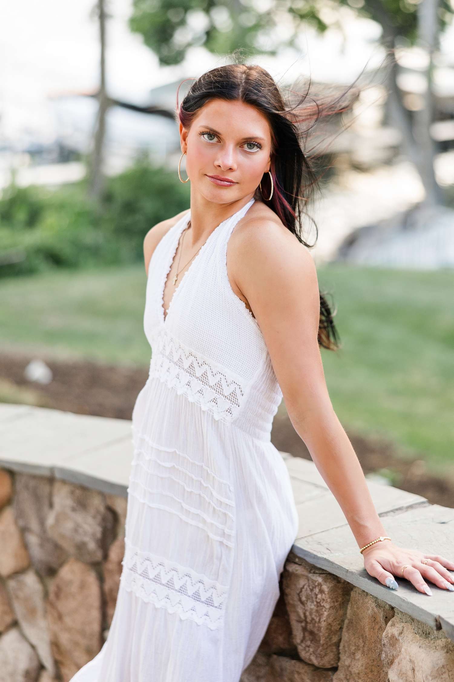 Brooke, wearing a long white linen dress, leans back on a stone stair case on West Okoboji Lake as the wind blows through her hair | CB Studio