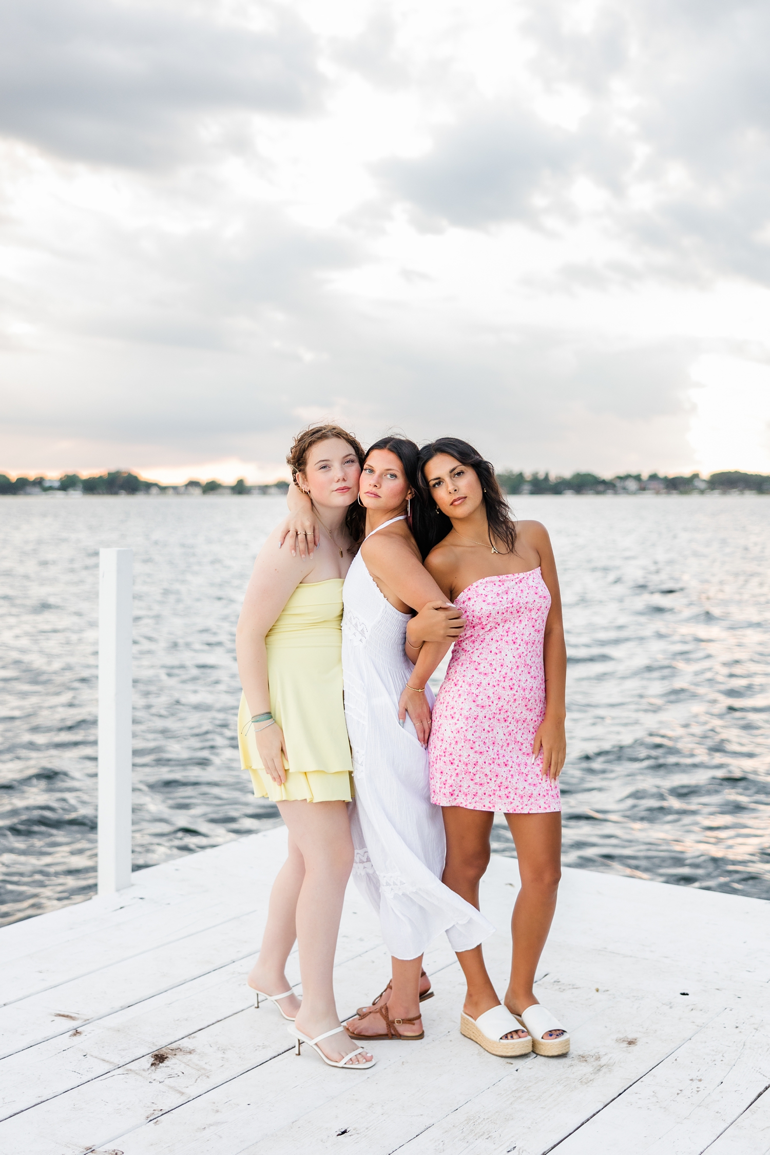Brooke and her two friends embrace as they stand on an all white dock on West Okoboji Lake | CB Studio