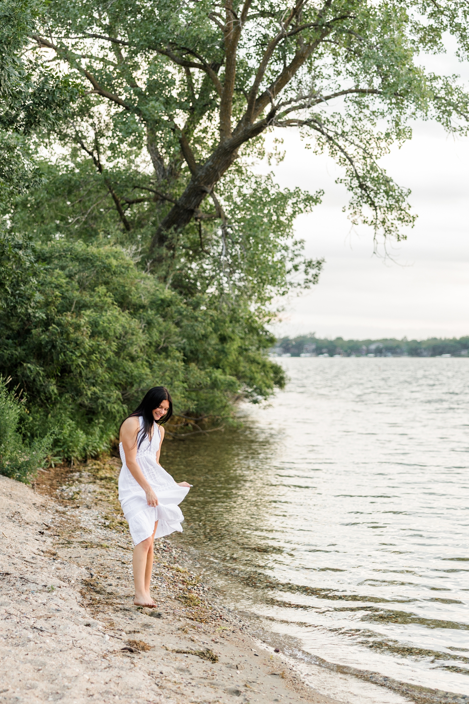 Brooke, wearing a long white linen dress, dances on the shore of West Okoboji Lake at Pikes Point State Park | CB Studio