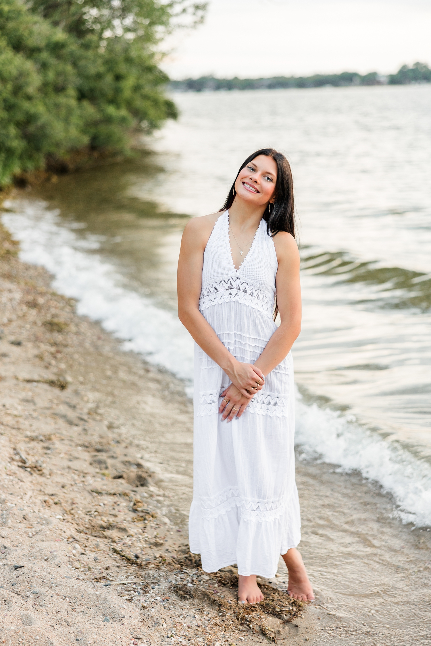 Brooke, wearing a long white linen dress, stands and smiles on the shore of West Okoboji Lake at Pikes Point State Park | CB Studio