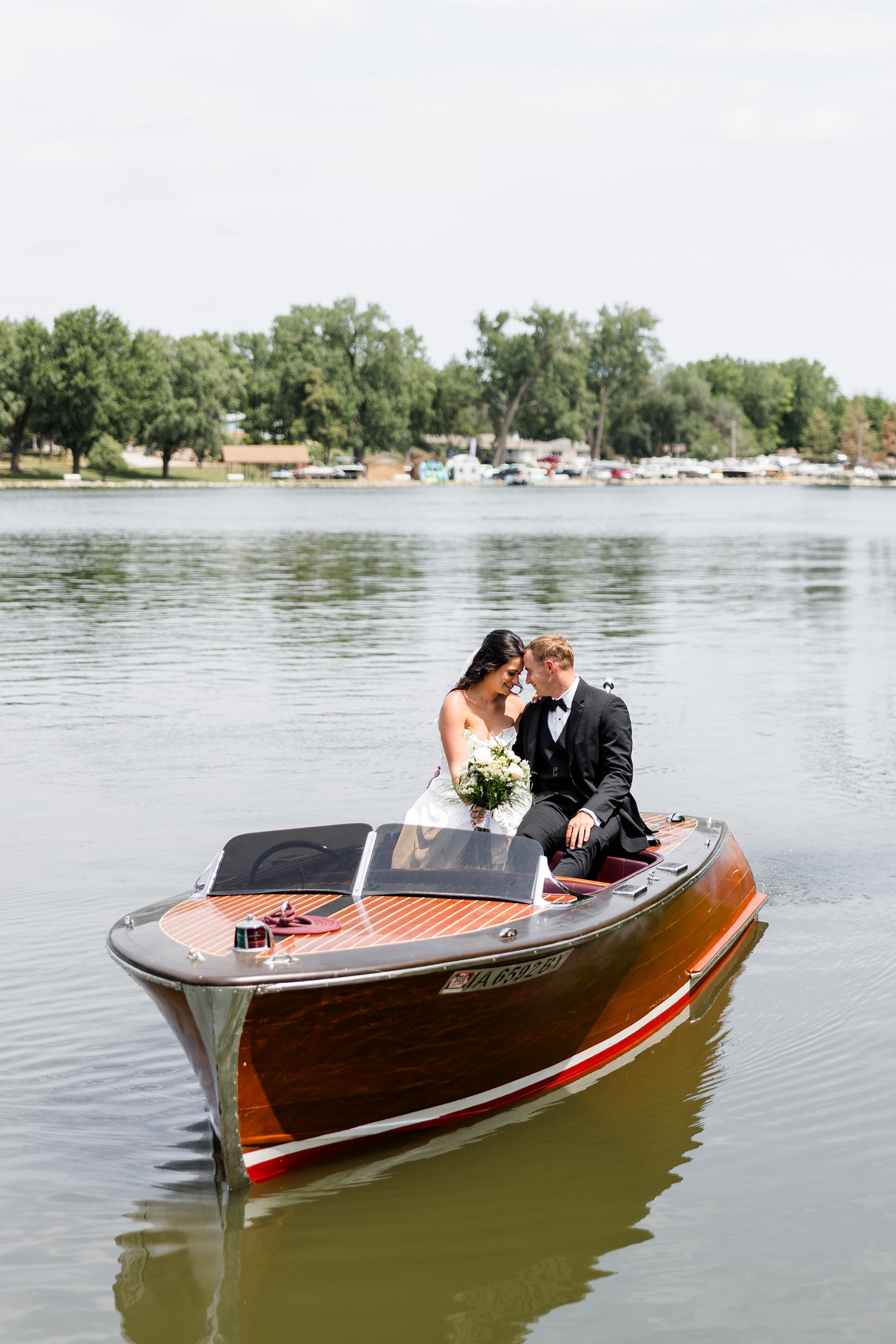 Bride and groom, Emily and Derrick, rests their heads together as they sit on the back of a Chris craft in the middle of Black Hawk Lake | CB Studio