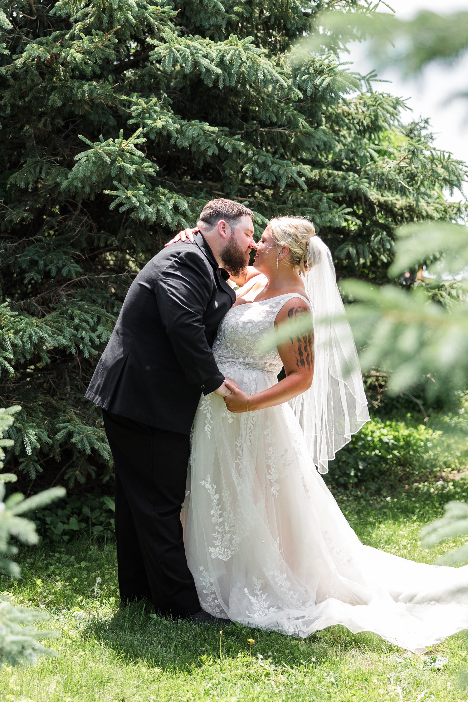 Teri and Dalton embrace and lean in for a kiss on their wedding day amongst the pines on their property | CB Studio