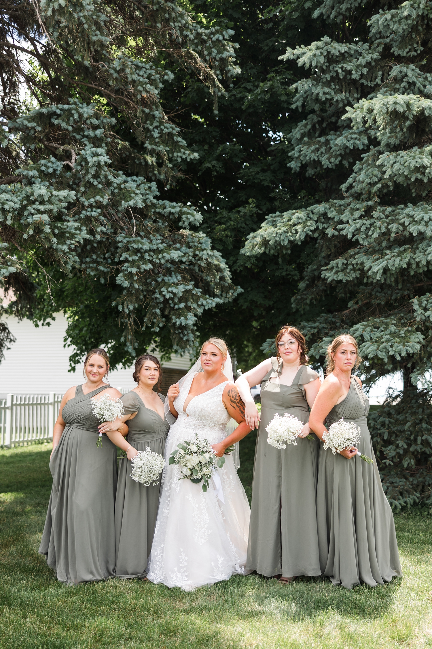 Teri and her bridesmaids, wearing sage green dresses and carrying baby's breath bouquets, pose in couture model poses beneath pine trees | CB Studio