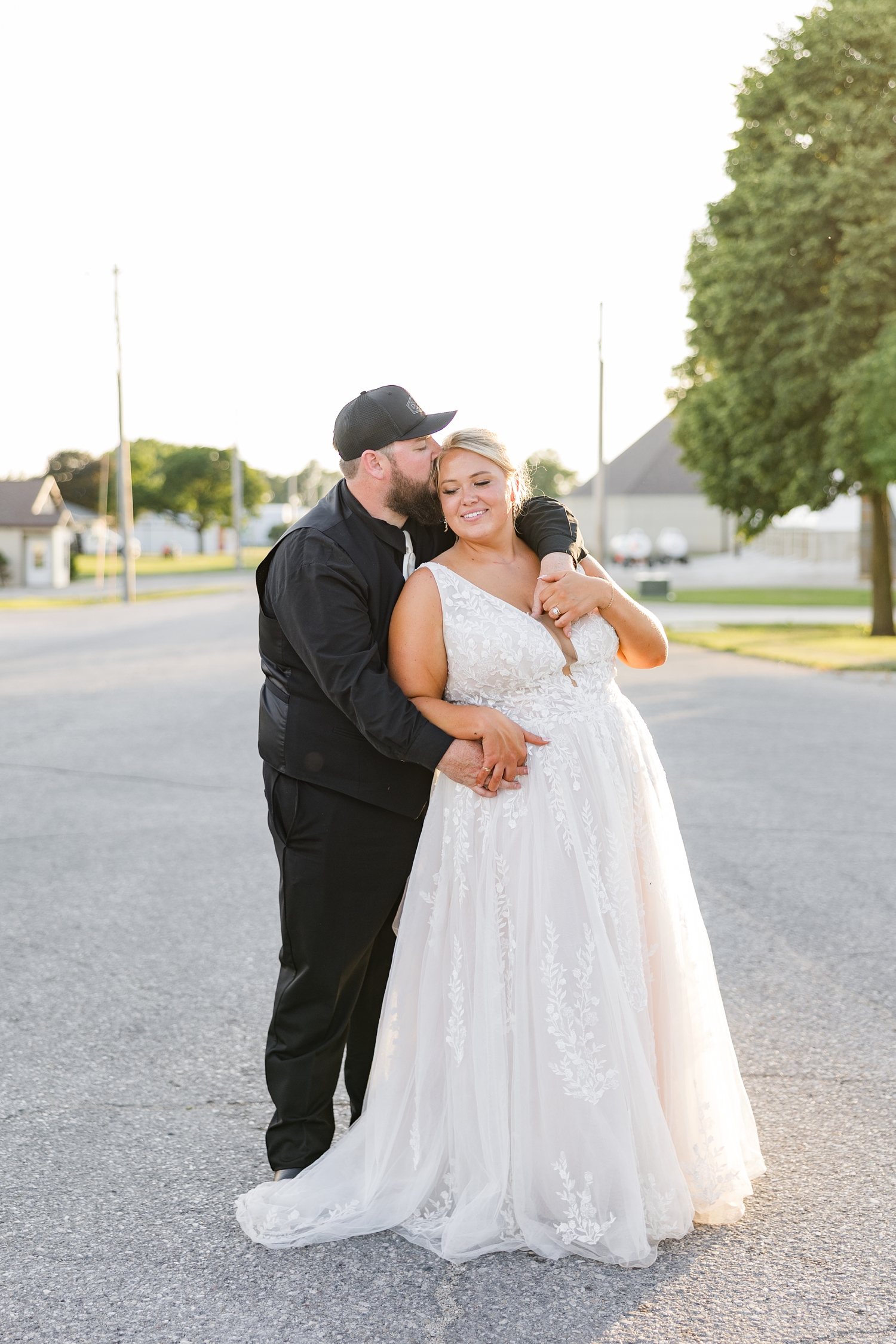 Dalton stands behind Teri as he embraces her and kisses her head on Main St. in Wesley, IA during golden hour | CB Studio