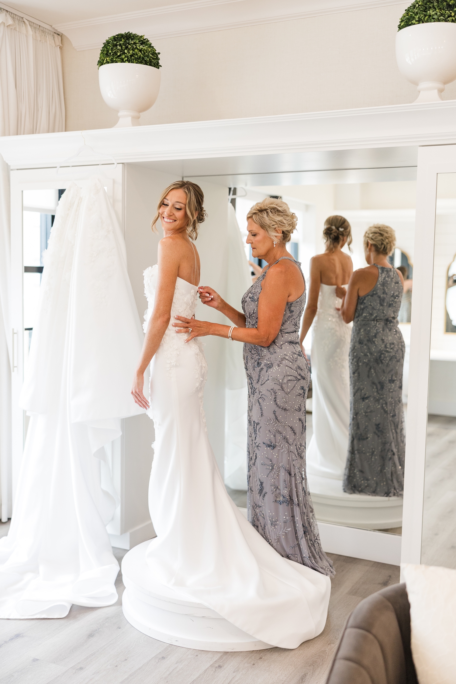 Cassidy's mom zips her into her wedding dress and they stand on a a pedestal in the all-white bridal suite at Toast in Ankeny, IA | CB studio