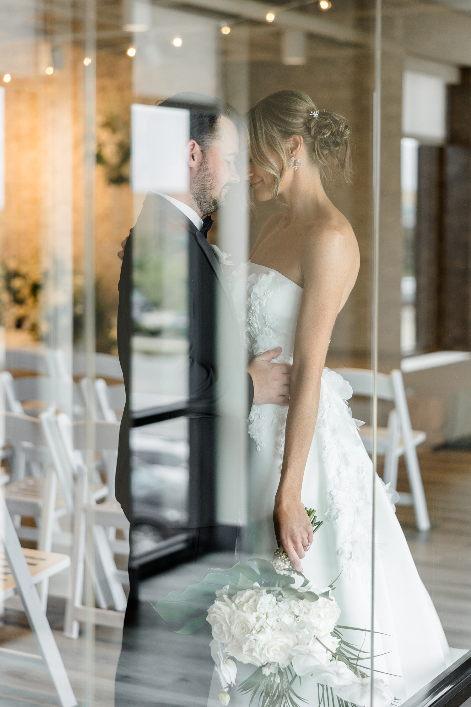 Cassidy and Grant rest their foreheads together behind a window with their wedding ceremony setup in the background at Toast in Ankeny, IA | CB studio