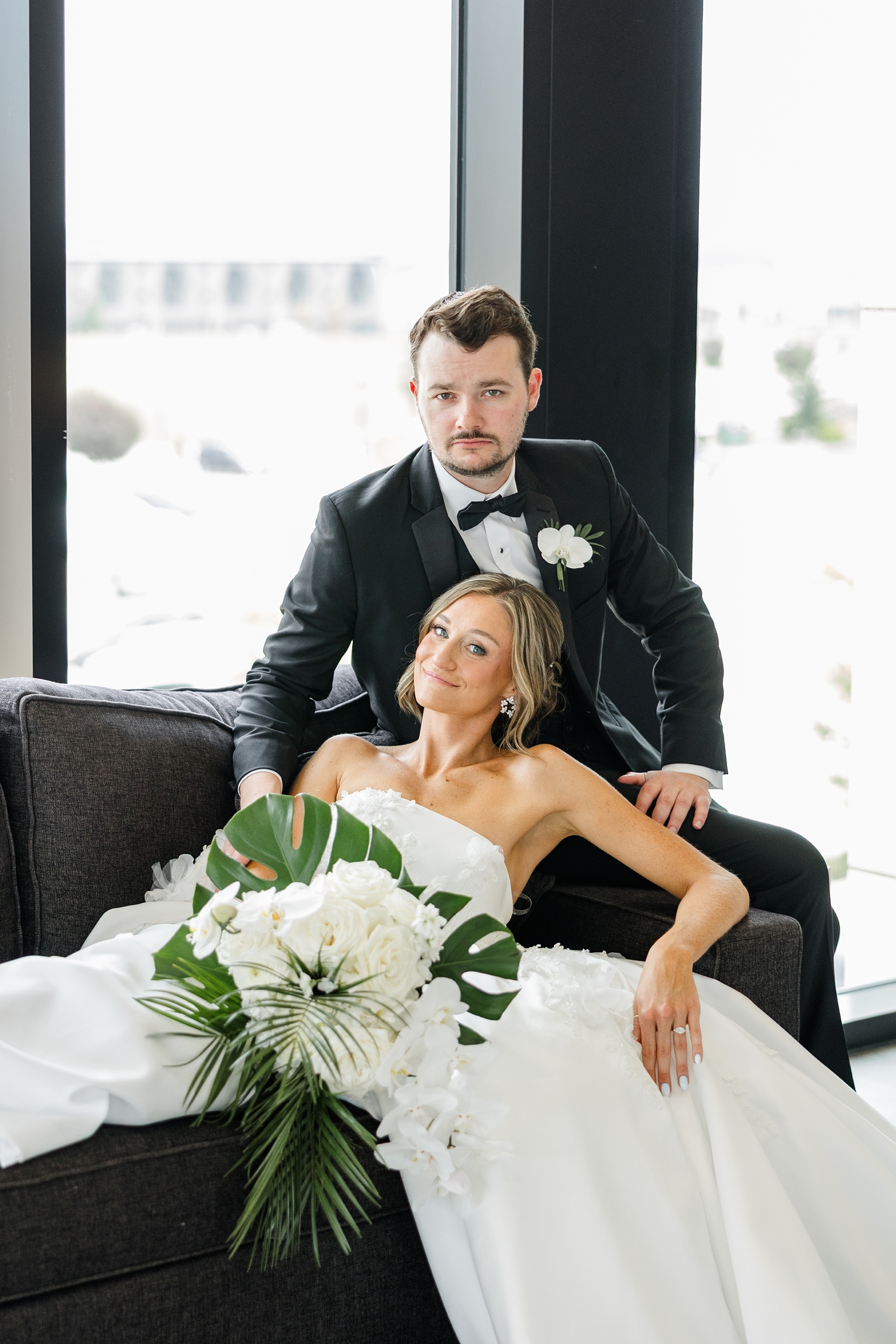 Cassidy lounges on a dark grey couch as Grant sits on the arm rest and leans over her at Toast in Ankeny, IA | CB Studio
