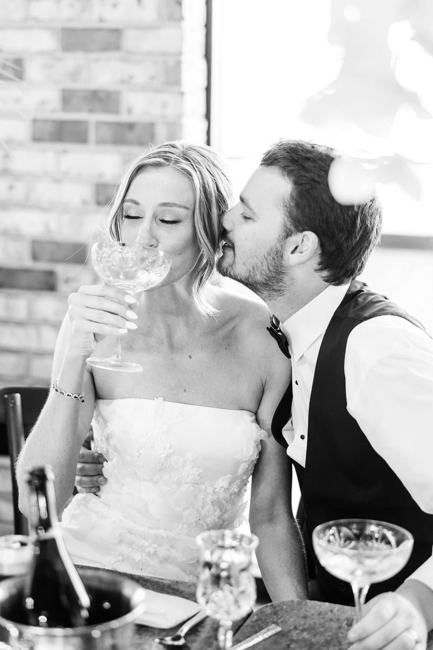 Cassidy sips wine from her crystal anniversary glass as Grant pulls her in for a kiss on the cheek at Toast in Ankeny, IA | CB Studio