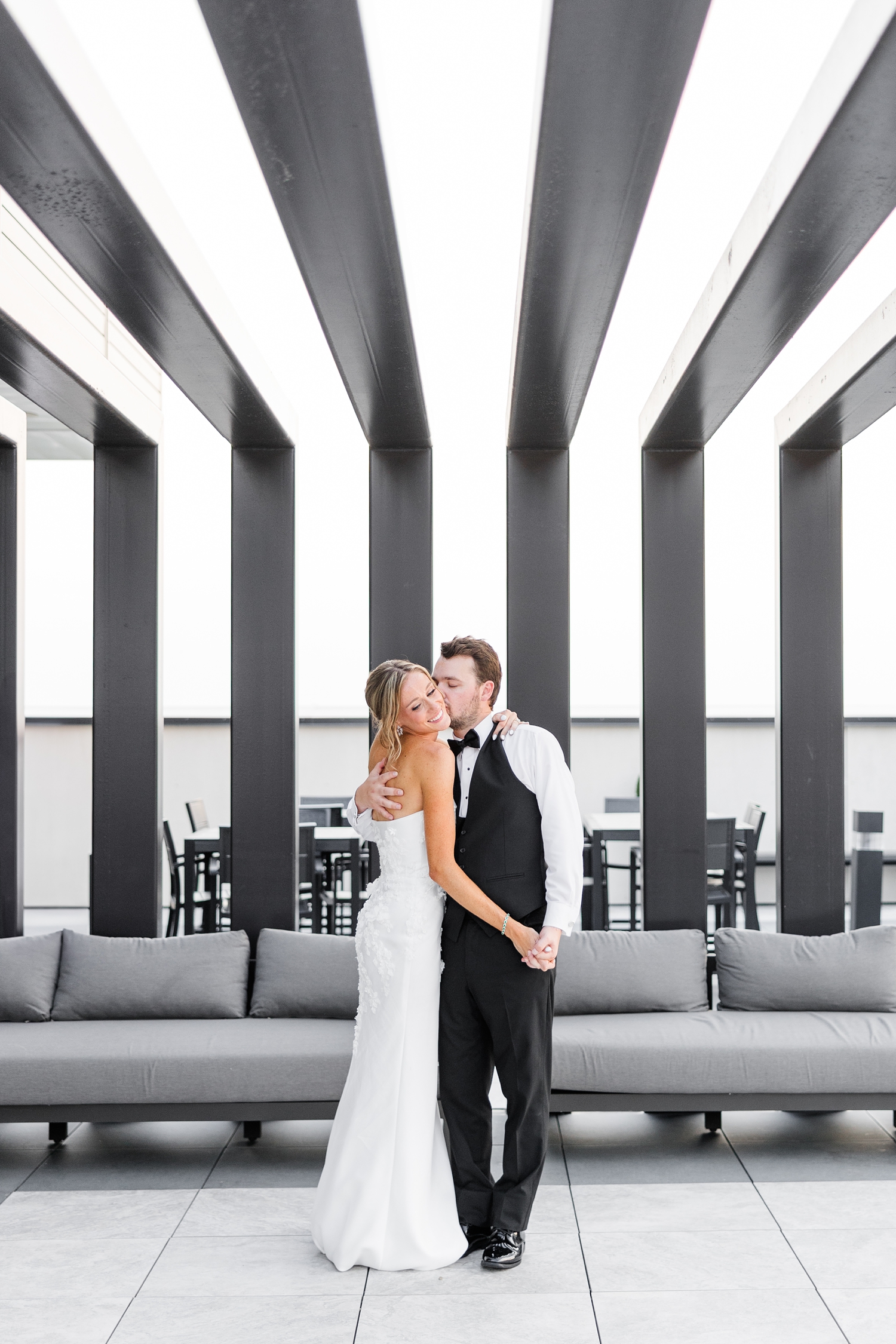 Grant holds his new bride's, Cassidy, hand and pulls her in for a kiss on the cheek under the iconic patio roof on the rooftop deck of Toast in Ankeny, IA | CB Studio