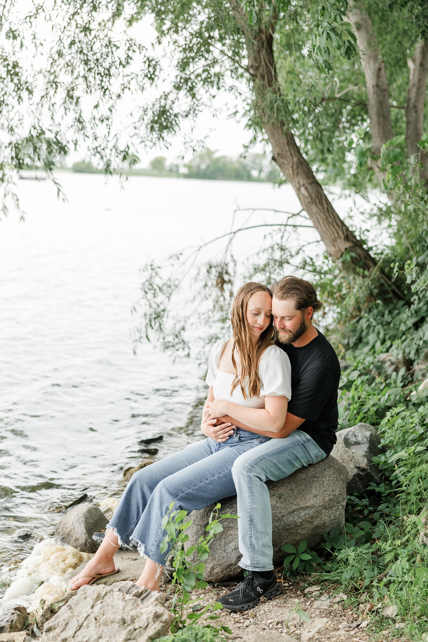 Chloe and Zach snuggle close together on a rock right next to Lake Cornelia | CB Studio