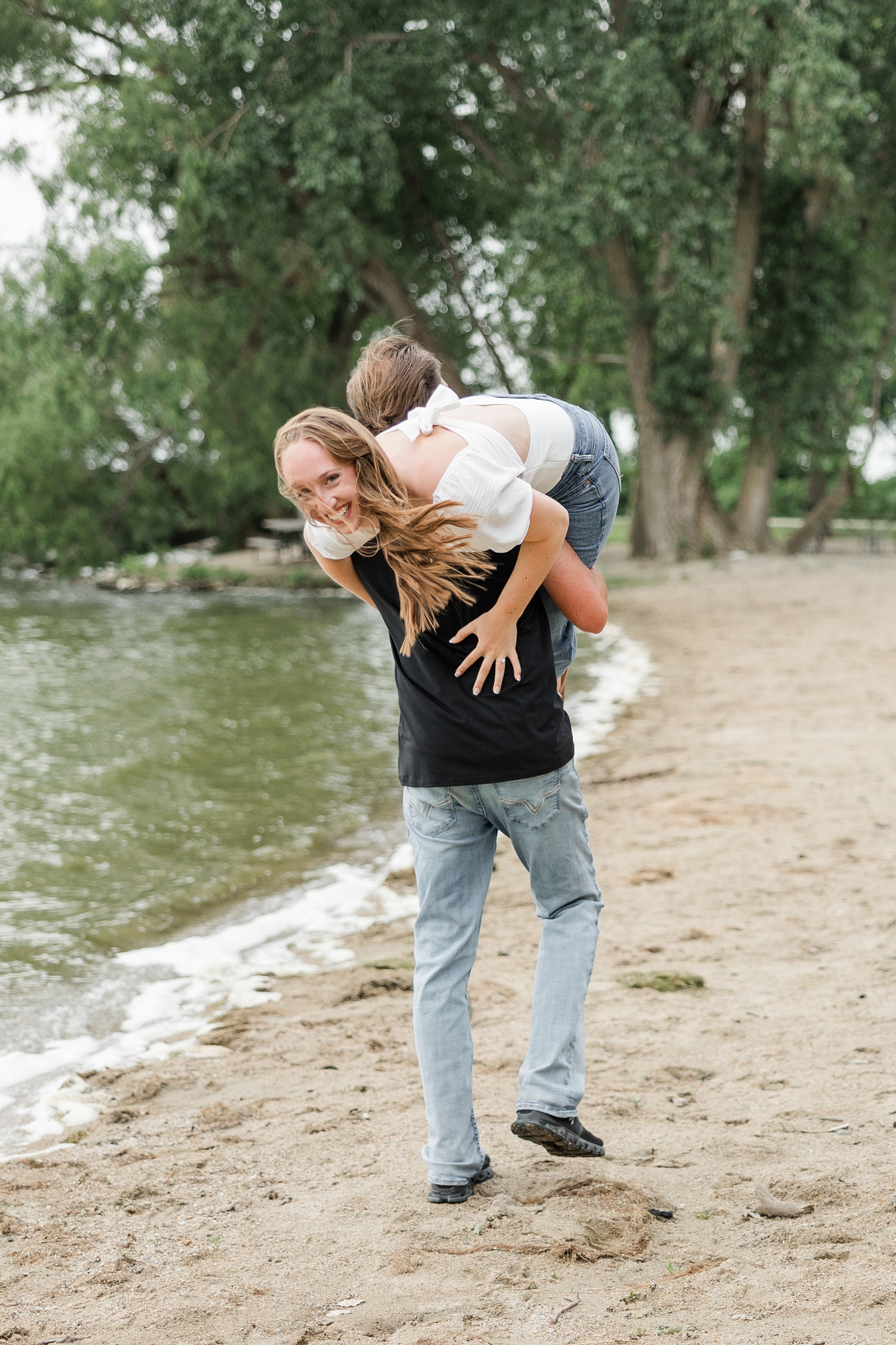 Zach picks Chloe up and throws her over his shoulder like a potato sack and carries her away on the beach of Lake Cornelia while Chloe laughs | CB Studio