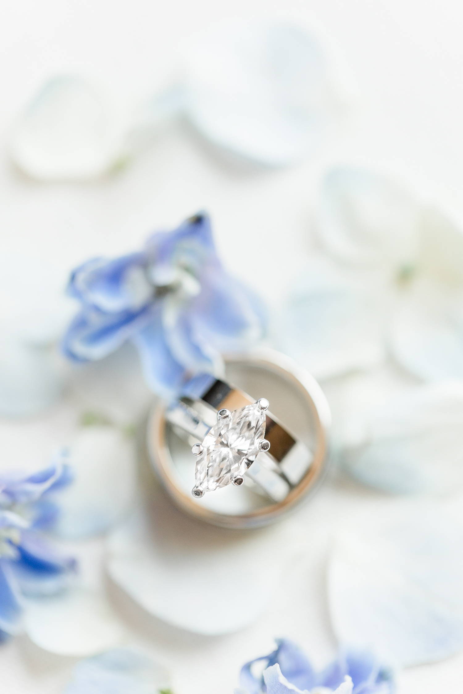 Large marquee diamond ring wand thick silver wedding band nestled inside a silver men's wedding band surrounded by blue hydrangea petals and other florals | CB Studio