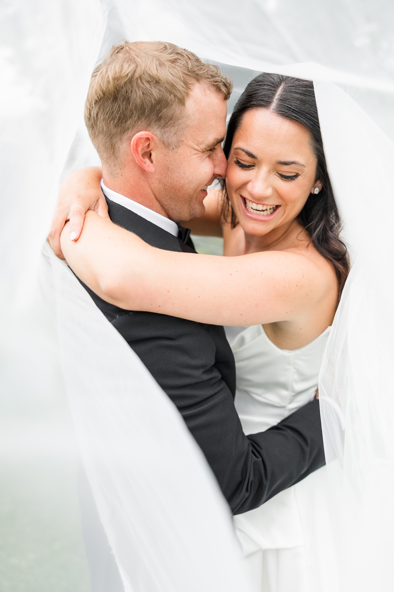Bride and groom, Emily and Derrick, embrace underneath Emily's cathedral length veil as Derrick gently nuzzles Emily while she laughs | CB Studio