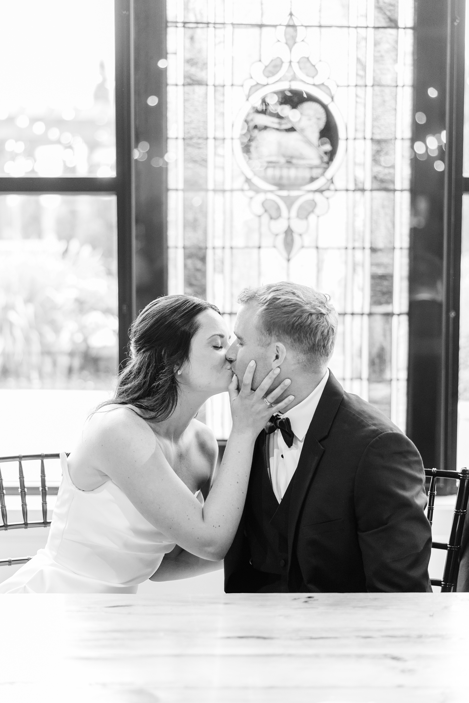 Emily grabs her husbands face and kisses him as they sit in front of the stained glass window at The Stables at Copper Ridge | CB Studio