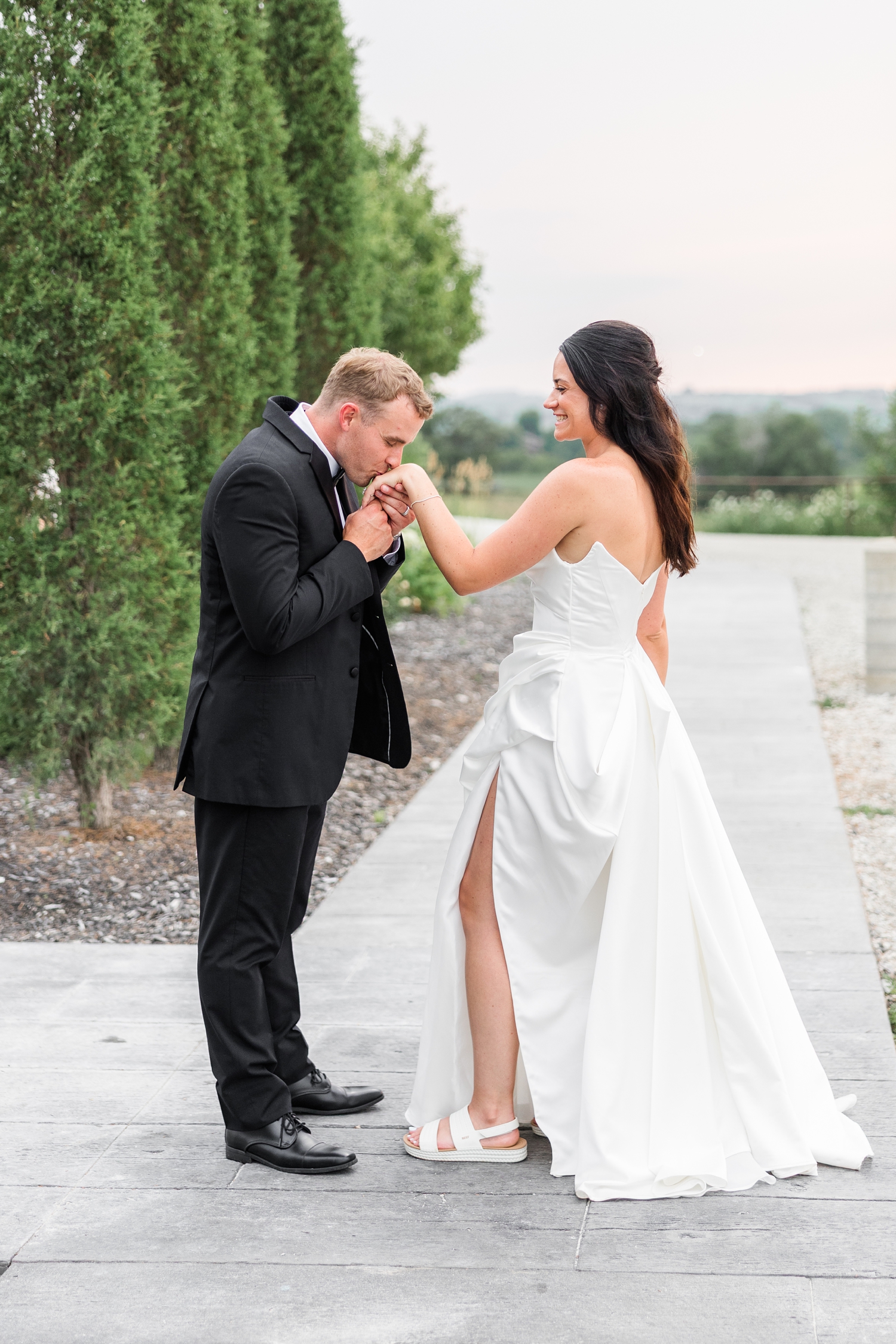 Derrick kisses his bride's hand, prince charming style, on a sidewalk at The Stables at Copper Ridge | CB Studio