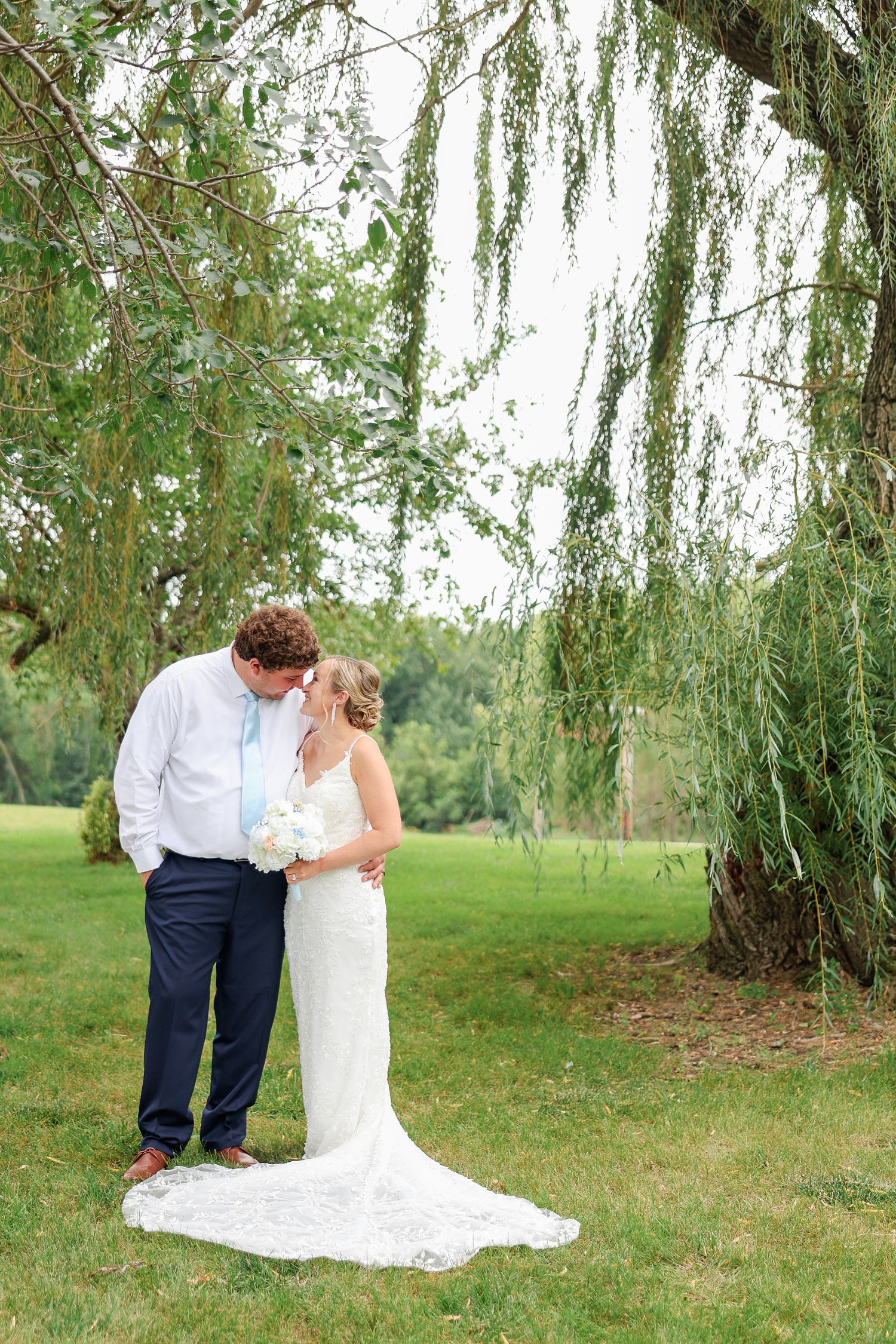 Surrounded by willow branches, Brandon and Alyssa side embrace and touch noses | CB Studio