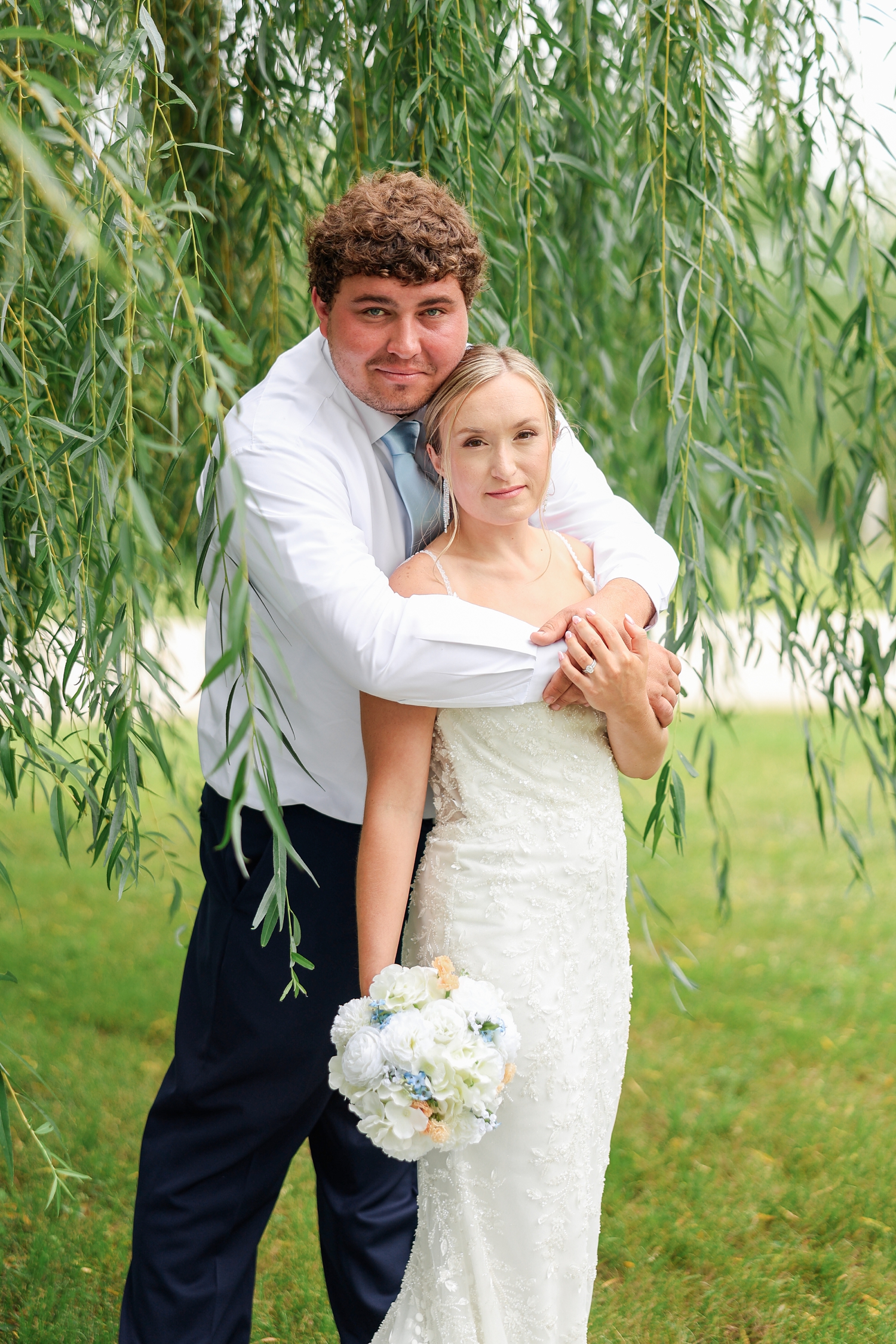 Surrounded by willow branches, Brandon hugs Alyssa from behind and model stare at the camera | CB Studio