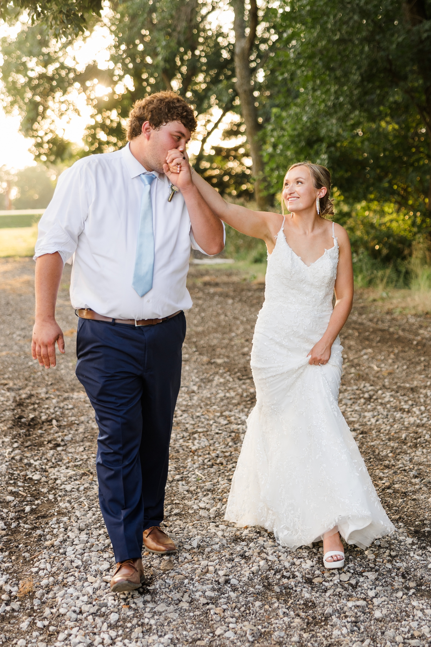 Brandon holds Alyssa's hand while they walk and brings it up to his mouth to kiss it all during golden hour along a row of trees | CB Studio