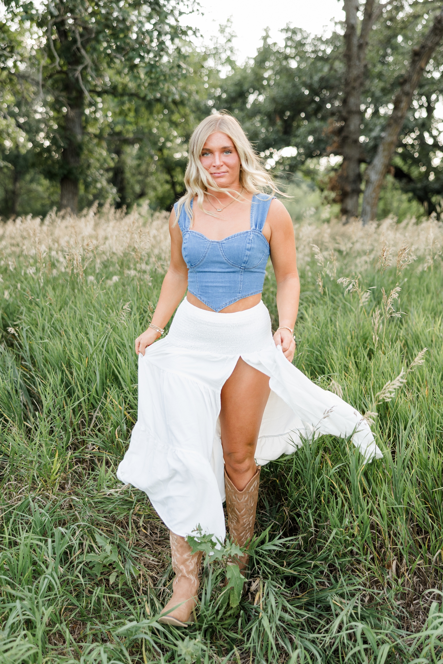 Audrey, wearing a white maxi skirt with a denim tank top, walks through a grassy field as the breeze slowly blows through her hair | CB Studio