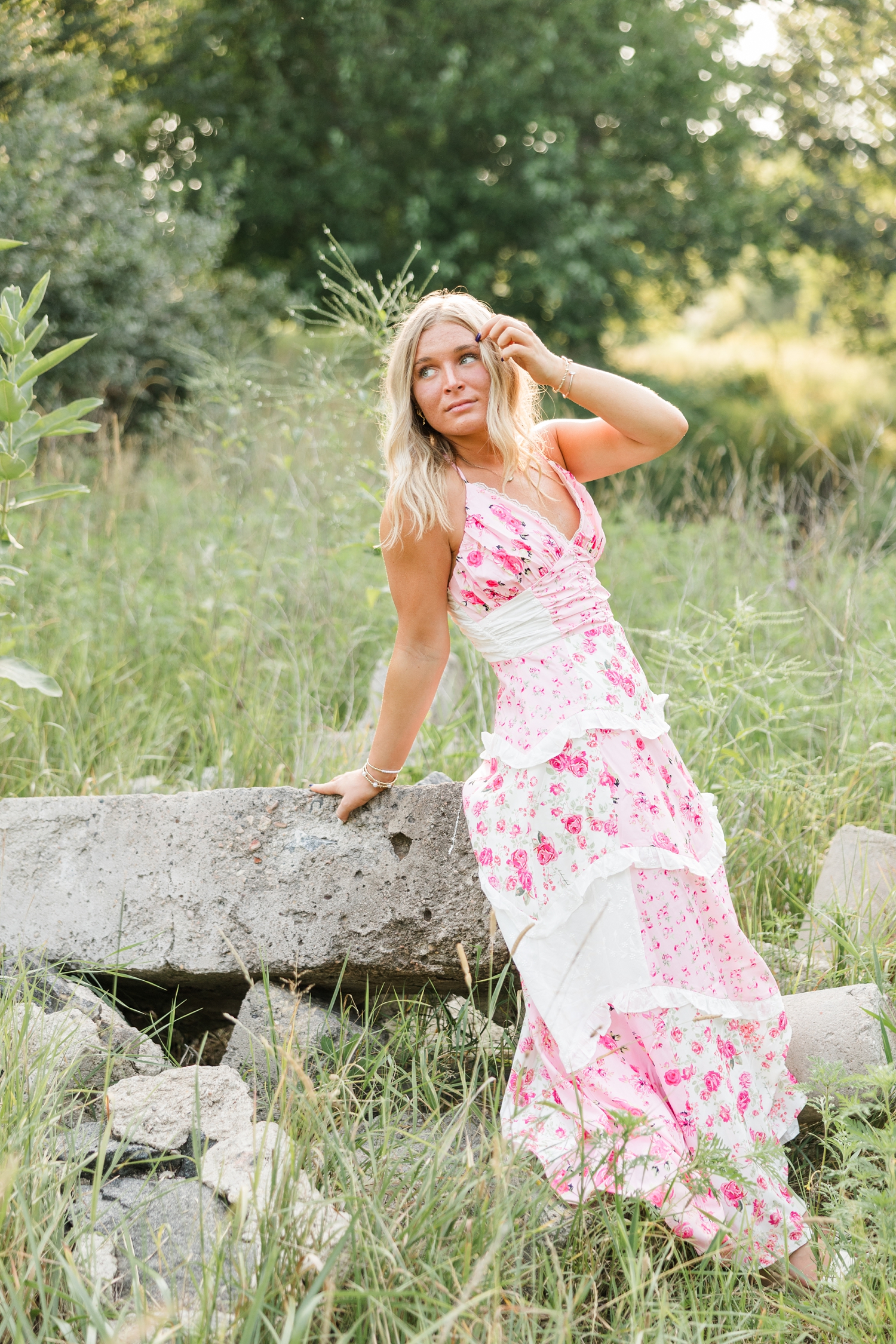 Audrey, wearing a pink and white patchwork/floral maxi dress, leans against a rock and looks looks to her left as she slowly tucks her hair behind her ear | CB Studio