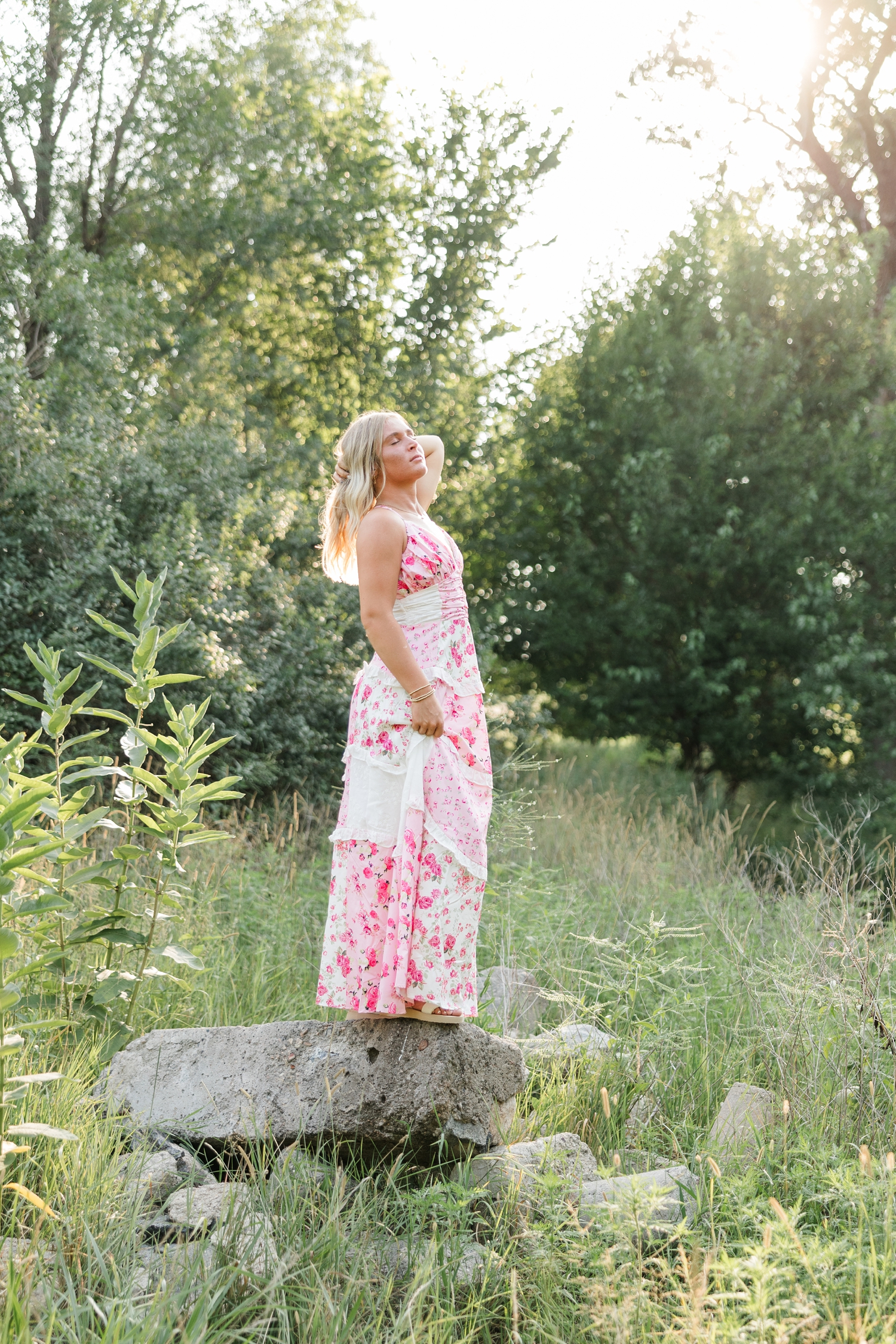Audrey, wearing a pink and white patchwork/floral maxi dress, stands on top of a rock and looks up as she grabs her hair and slowly lets it fall | CB Studio