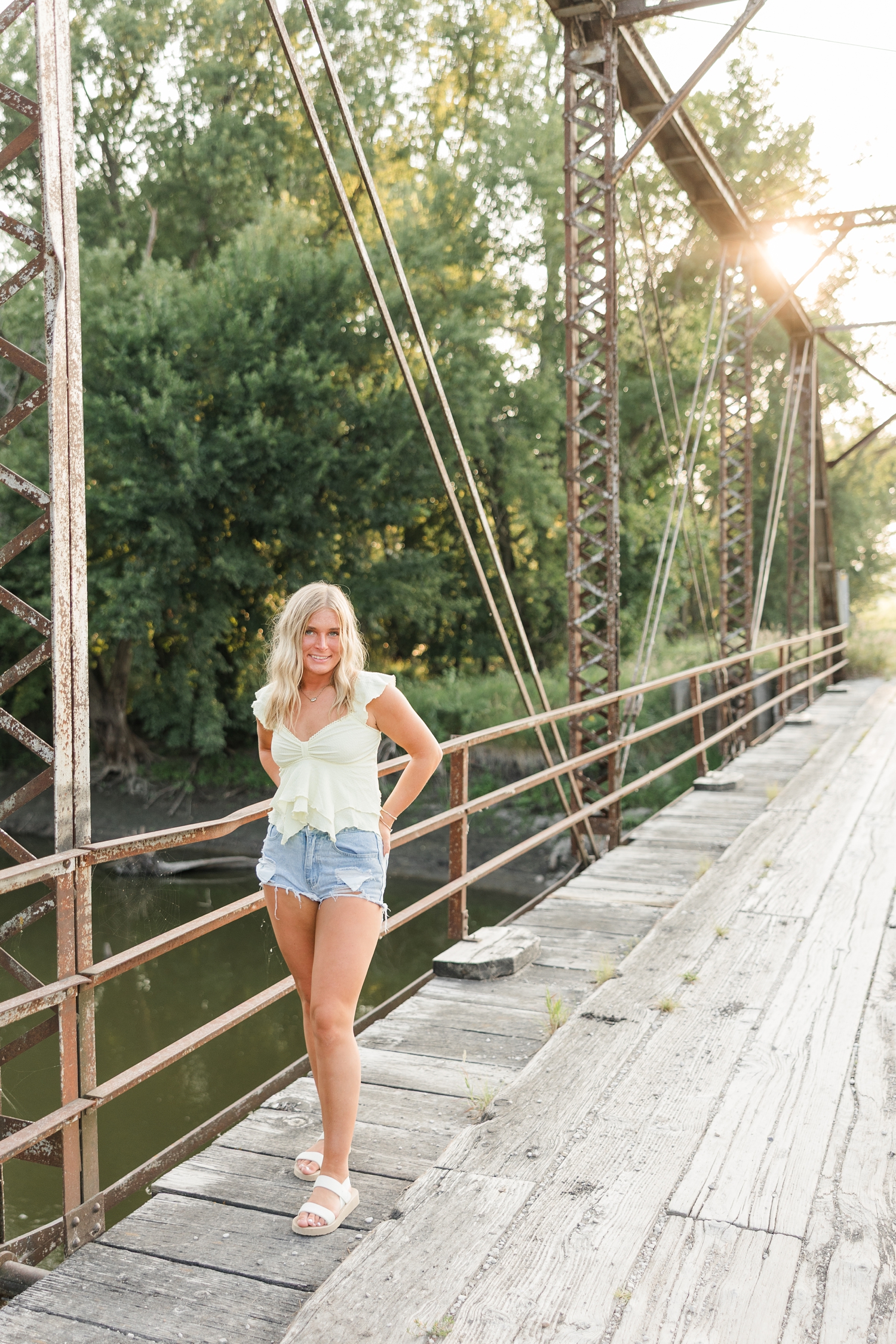 Audrey, wearing a butter yellow flowy top and denim shorts, walks along an old trestle bridge as the sun sets | CB Studio