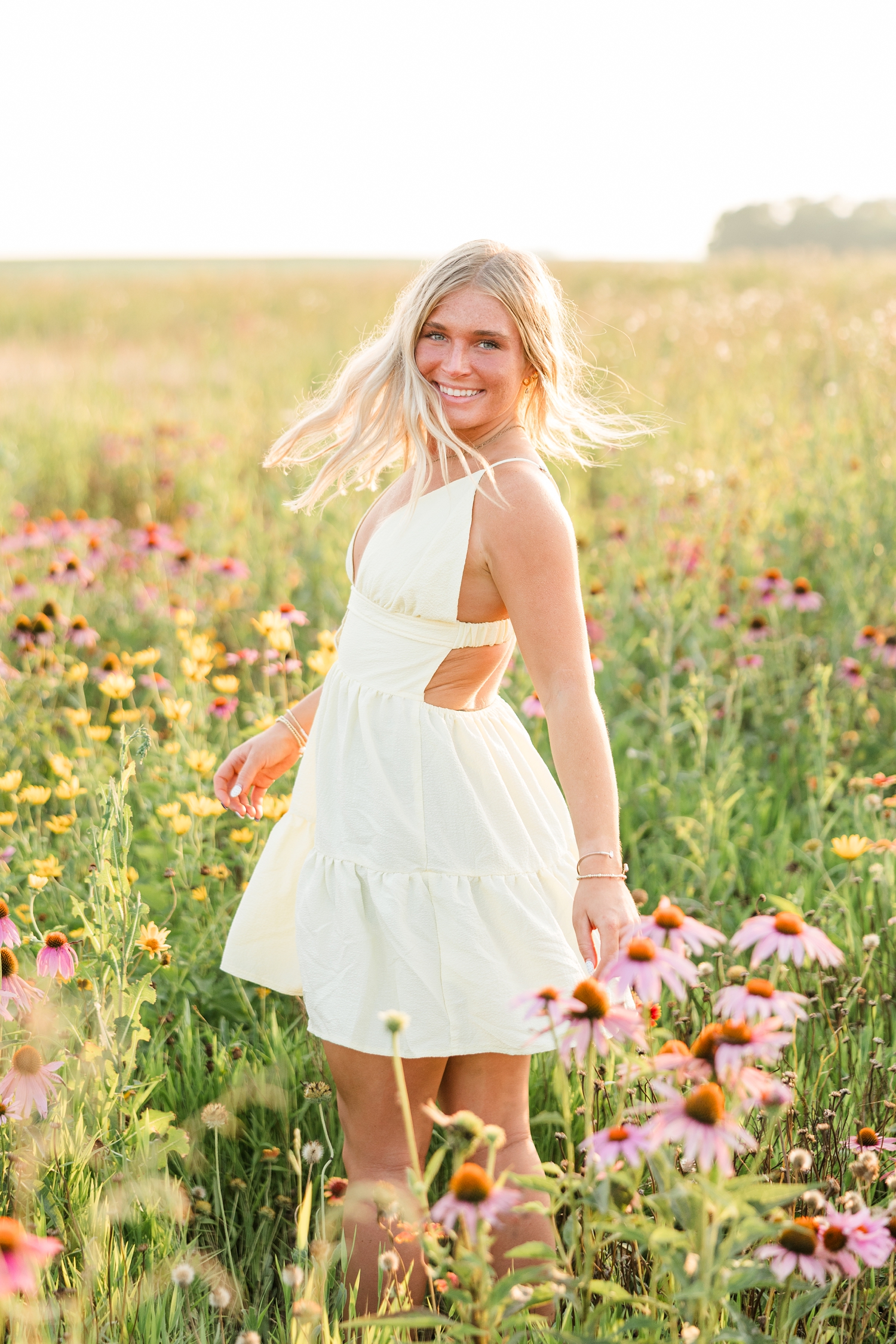 Audrey, wearing a mini butter yellow sundress, spins from side to side in a wildflower field during golden hour with her hair and skirt twirling to the movement | CB Studio