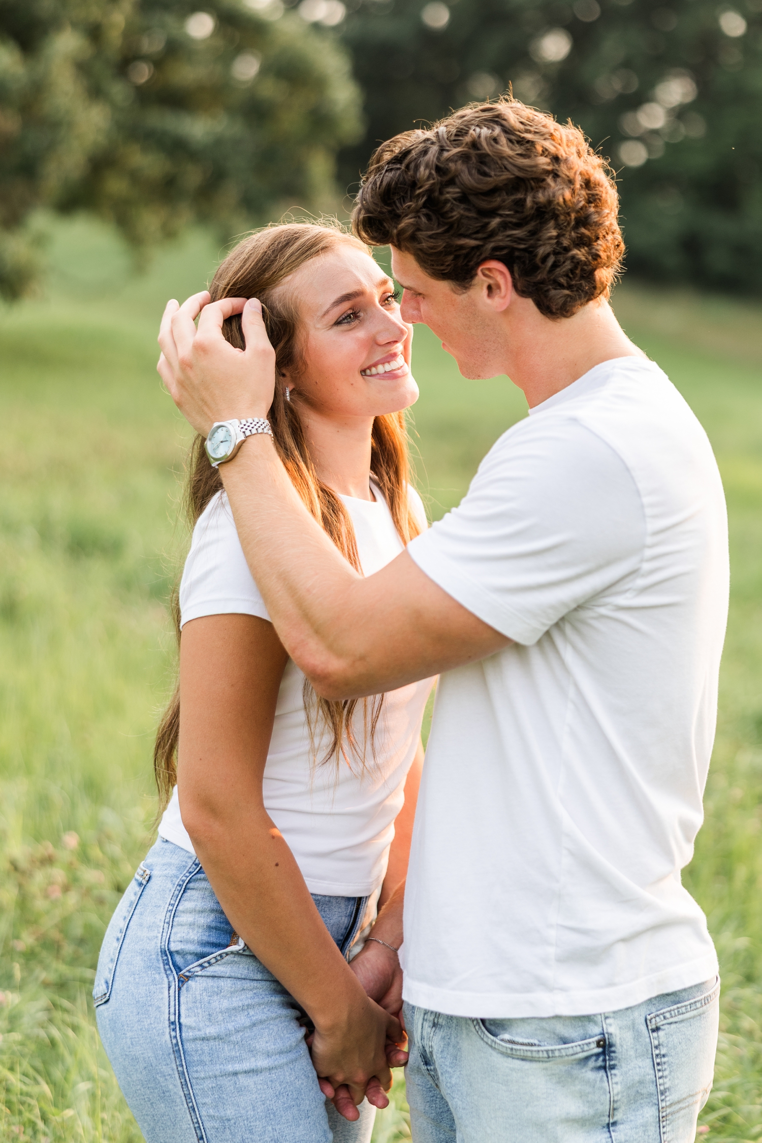 Tyler slowly tucks Deni's (both wearing jeans and a white t-shirt) hair behind her ear in the middle of a grass pasture | CB Studio