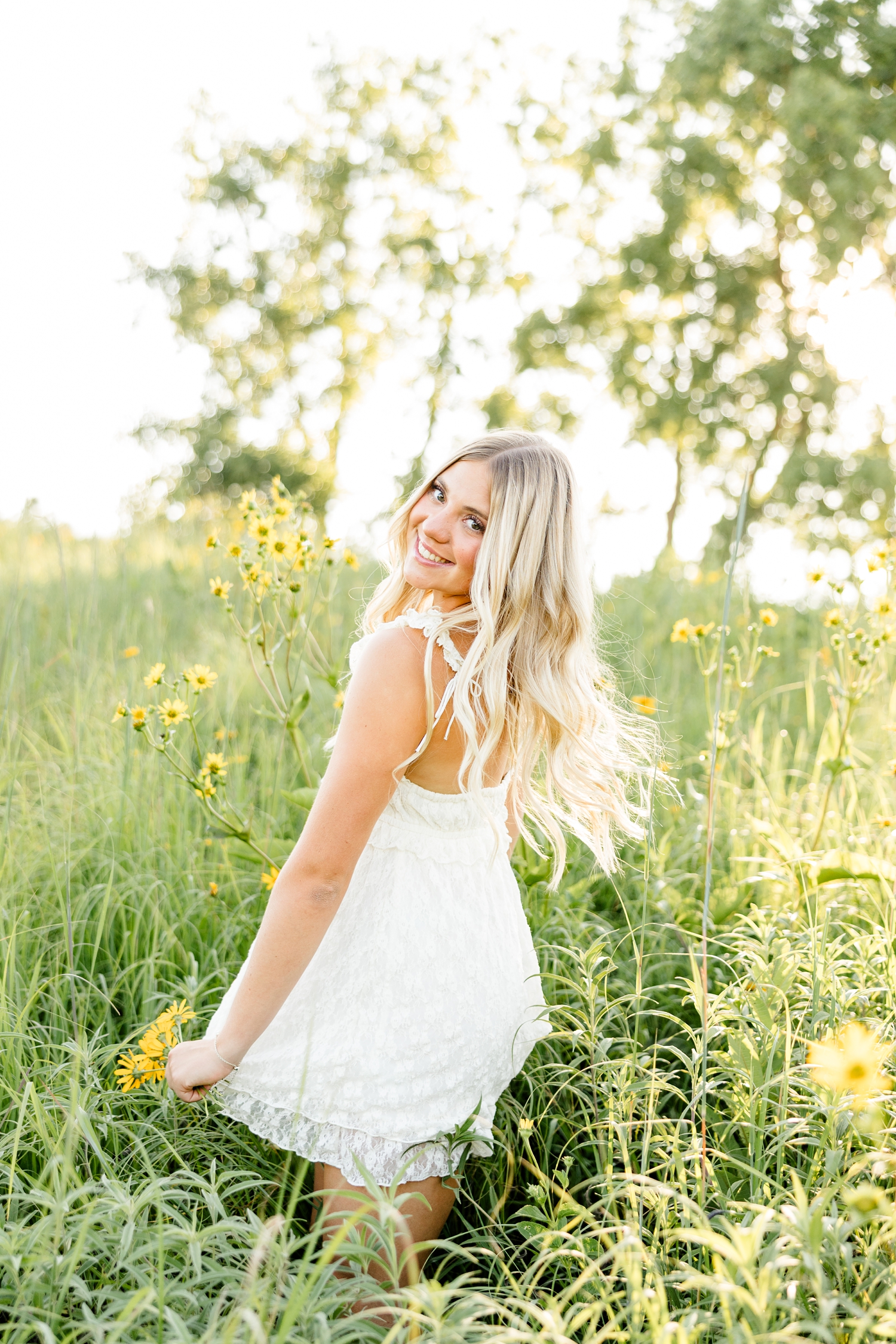 Emma, wearing a cream lace dress, spins in a yellow flower field at golden hour while looking over her shoulder and smiling | CB Studio