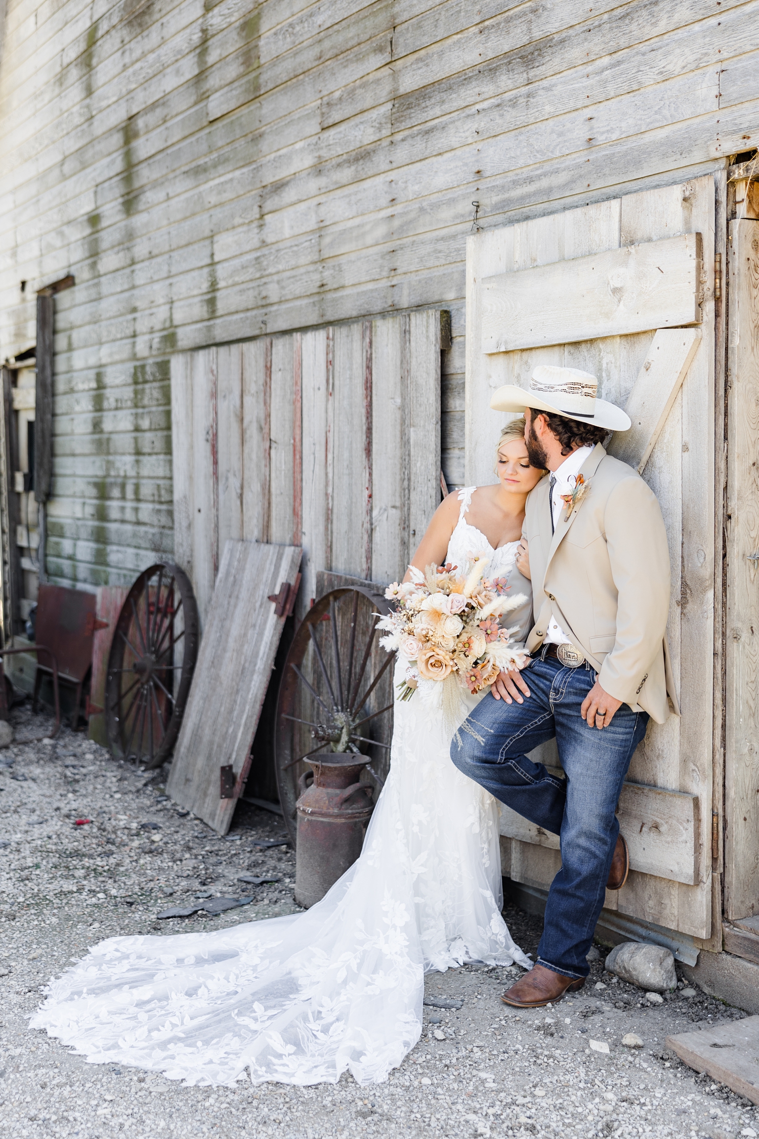 Dawson leans against an old wooden barn while Jade hugs his arm and rests her cheek on his shoulder and he kisses her forehead | CB Studio