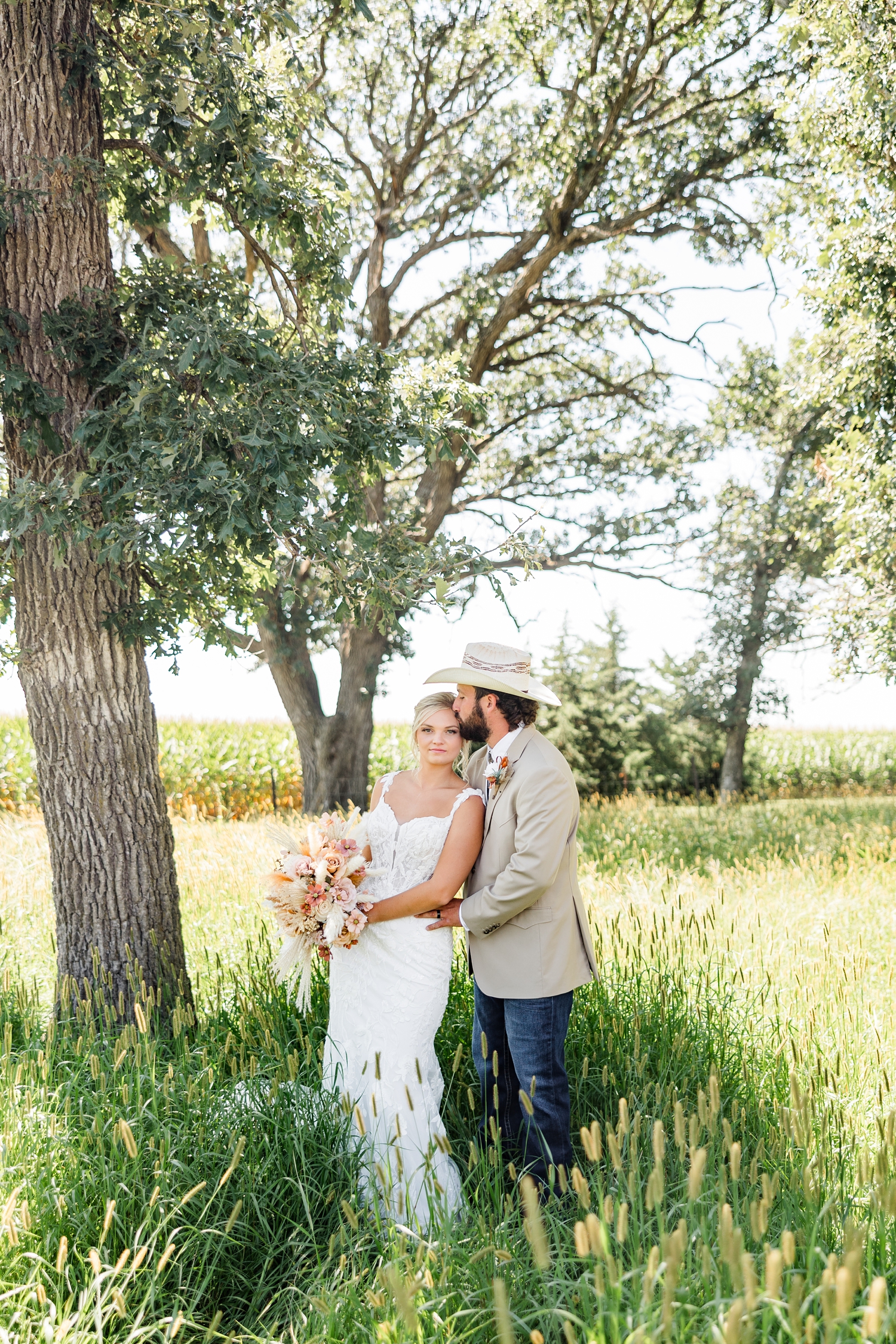 Dawson holds Jade's waist and kisses her forehead as they stand out in the middle of a grass pasture | CB Studio