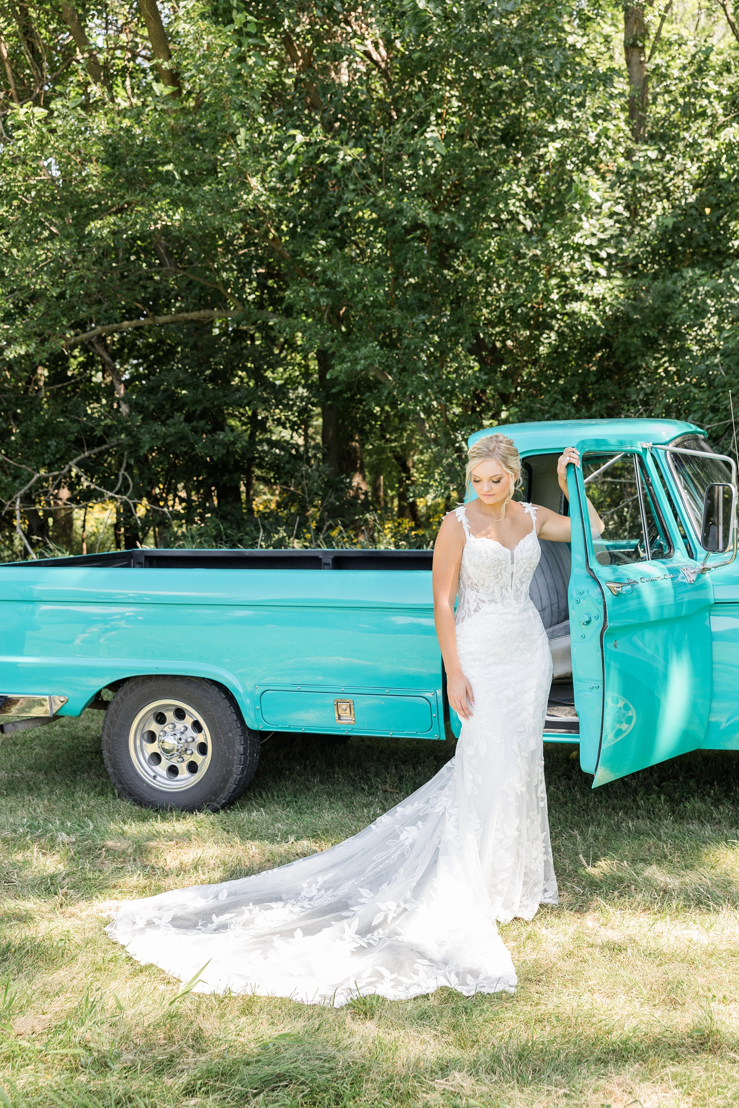 Jade leans her arm on the open passenger side door of an old restore turquoise Ford truck and looks down at her wedding gown train laying on the ground in front of her | CB Studio