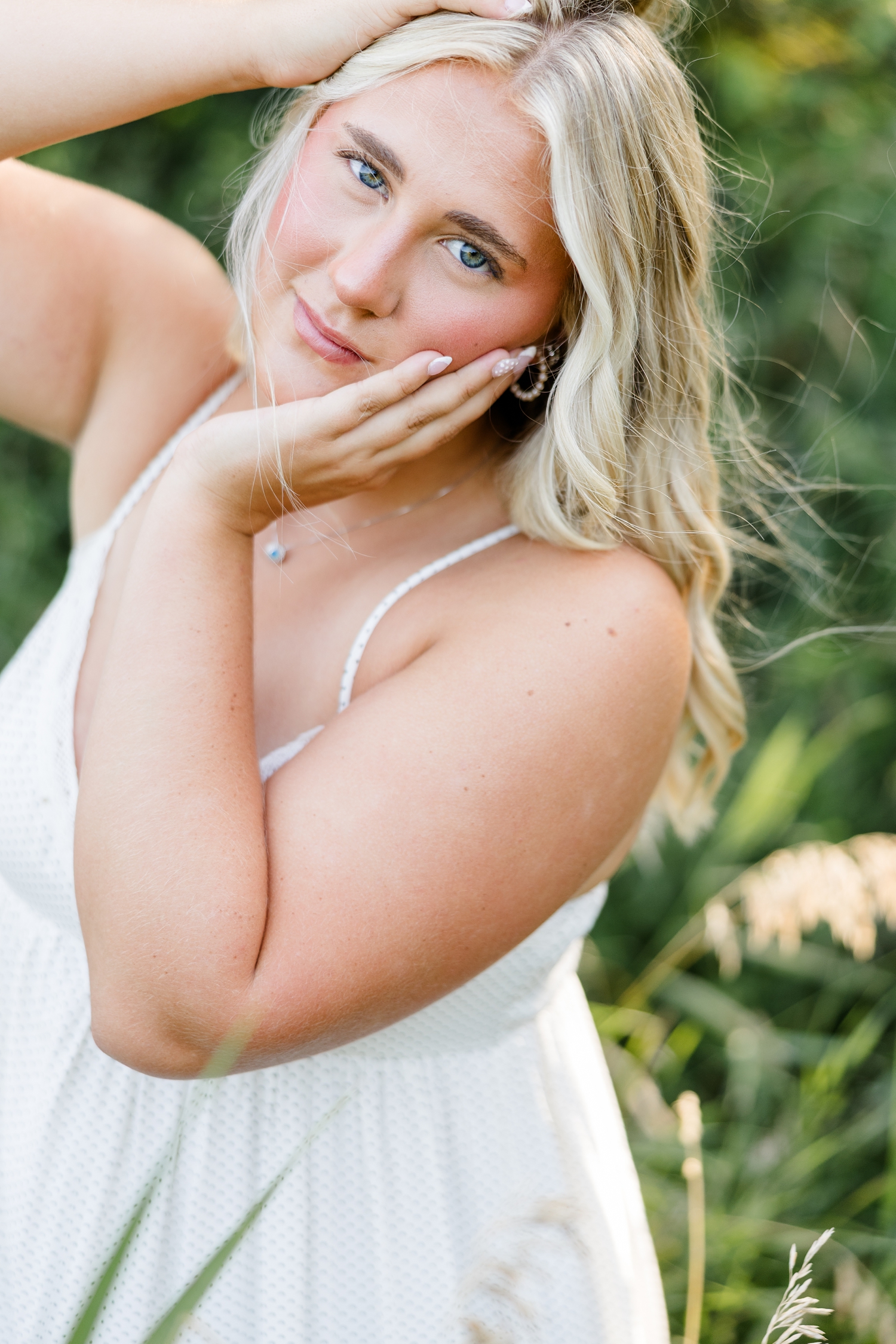 Ocean, wearing a white sundress, stands in a grassy meadow while framing her face and head with her hands | CB Studio