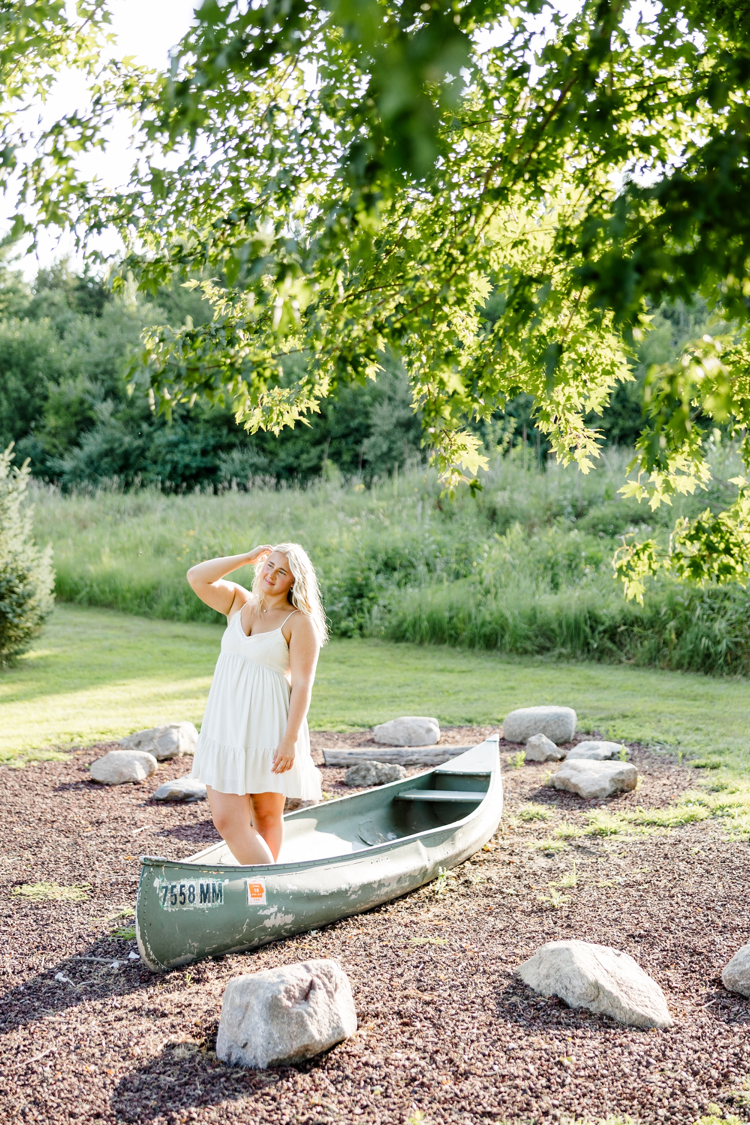 Ocean, wearing a white sundress, stands in a canoe display at Water's Edge Nature Center while she slowly tucks her hair behind her ear | CB Studio