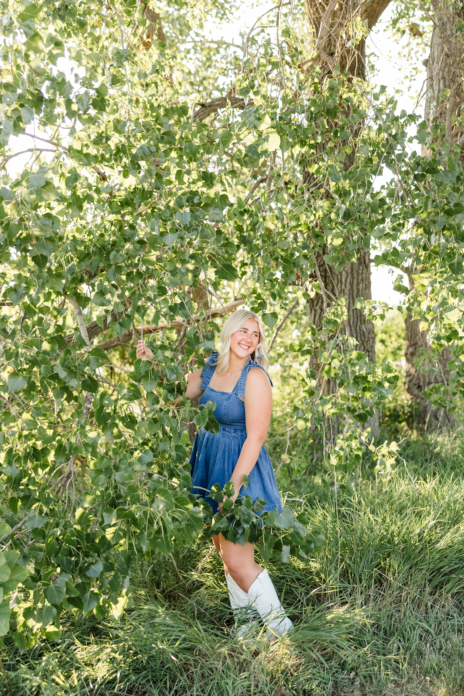 Ocean, wearing a denim dress, stands among the branches of a birch tree as she she laughs while looking over her right shoulder | CB Studio