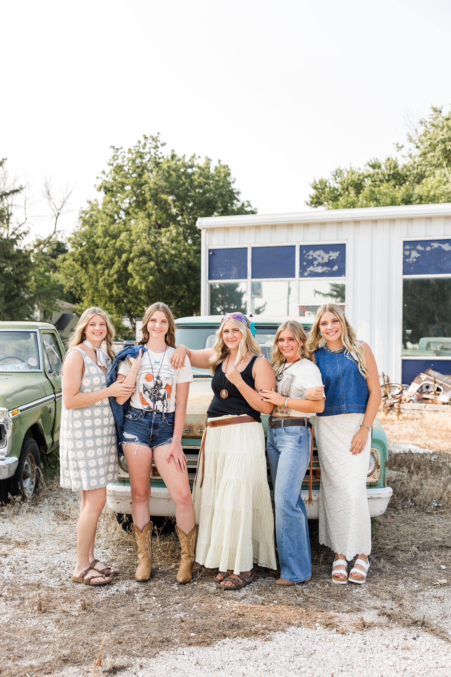 TEAM 27, dressed in boho, grunge looks, stand in model poses in front of an old rustic truck at a broken down gas station | CB Studio