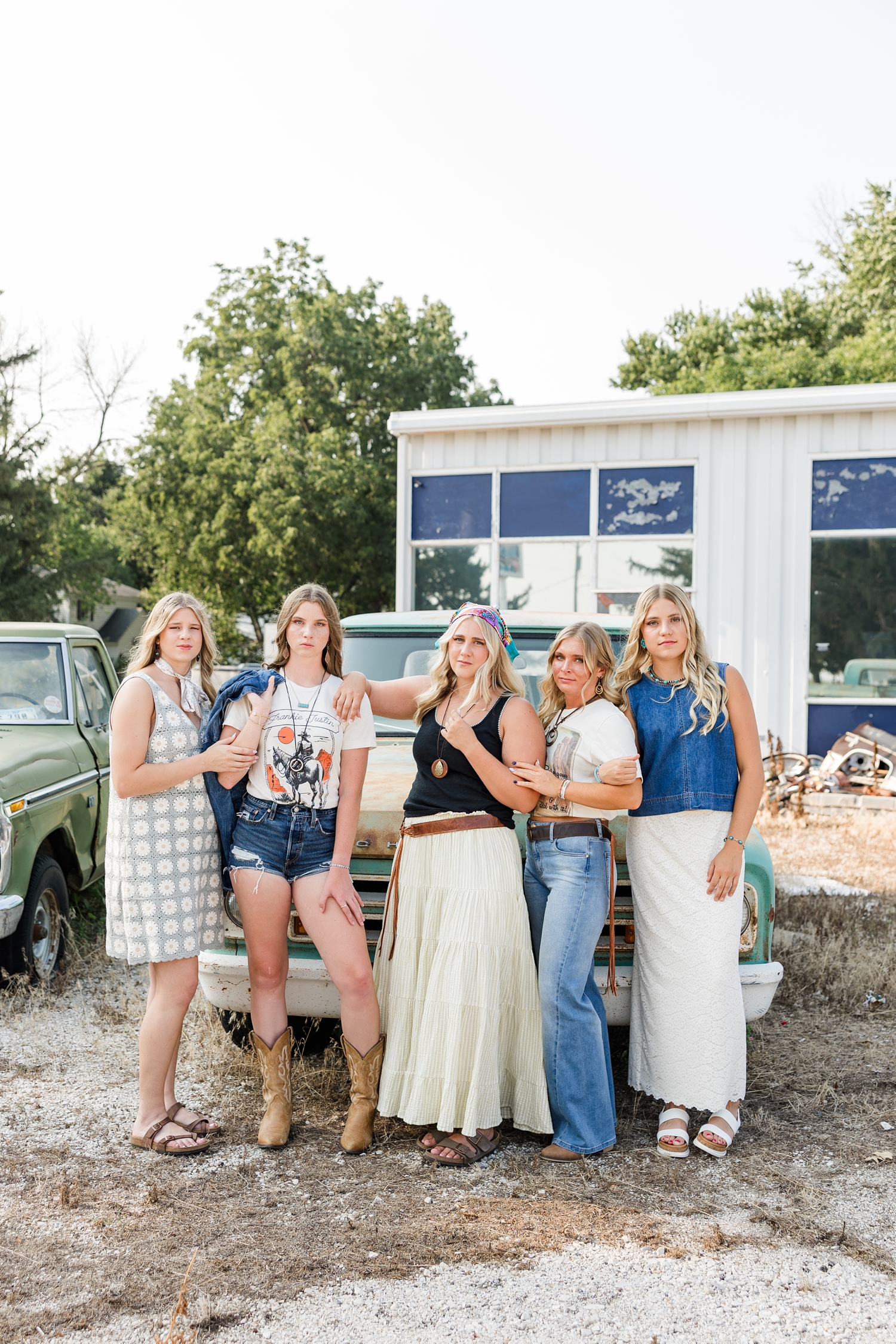 TEAM 27, dressed in boho, grunge looks, stand in model poses in front of an old rustic truck at a broken down gas station | CB Studio