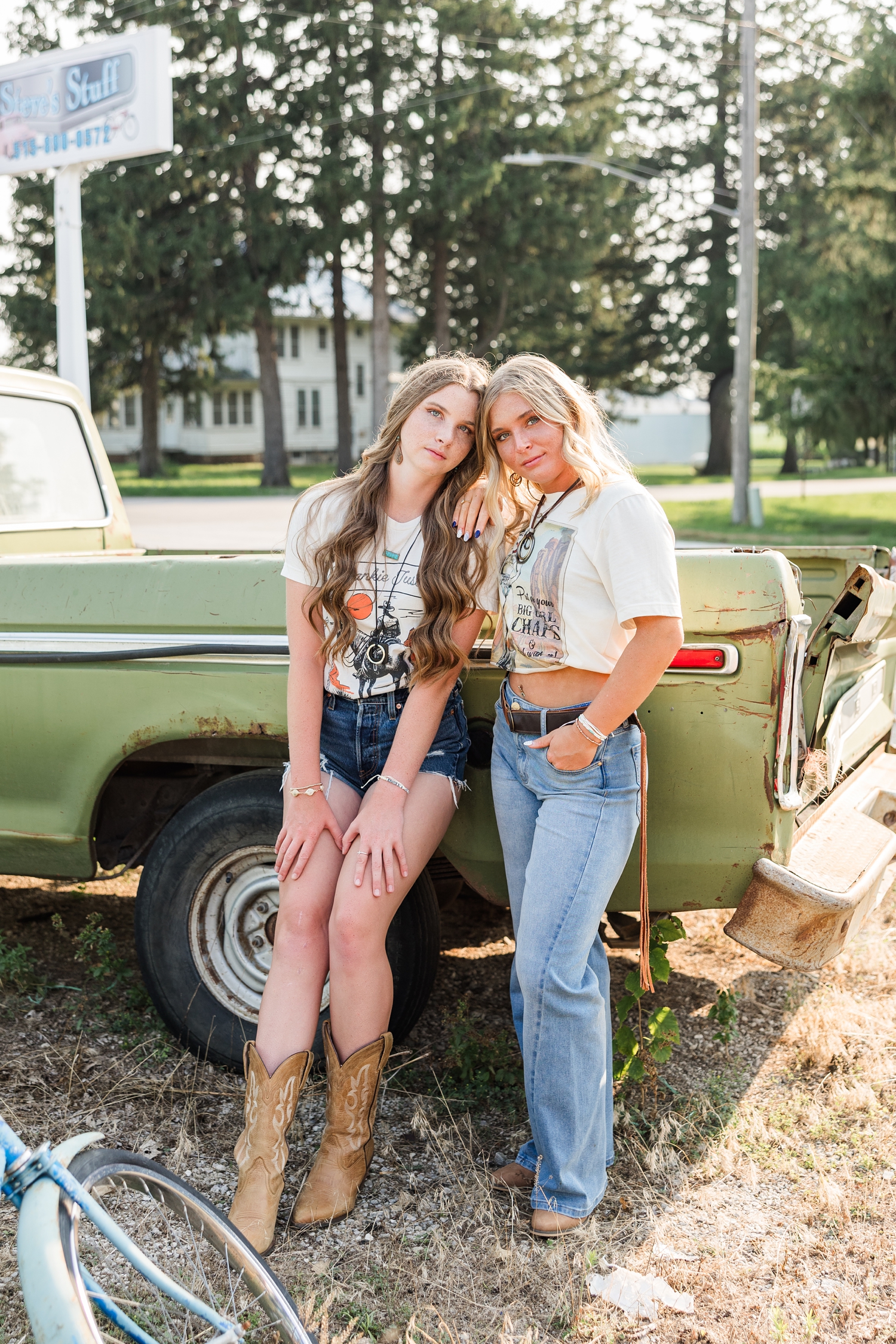 Mya and Audrey, dressed in boho, grunge looks, stand in model poses in front of an old rustic truck at a broken down gas station at golden hour | CB Studio