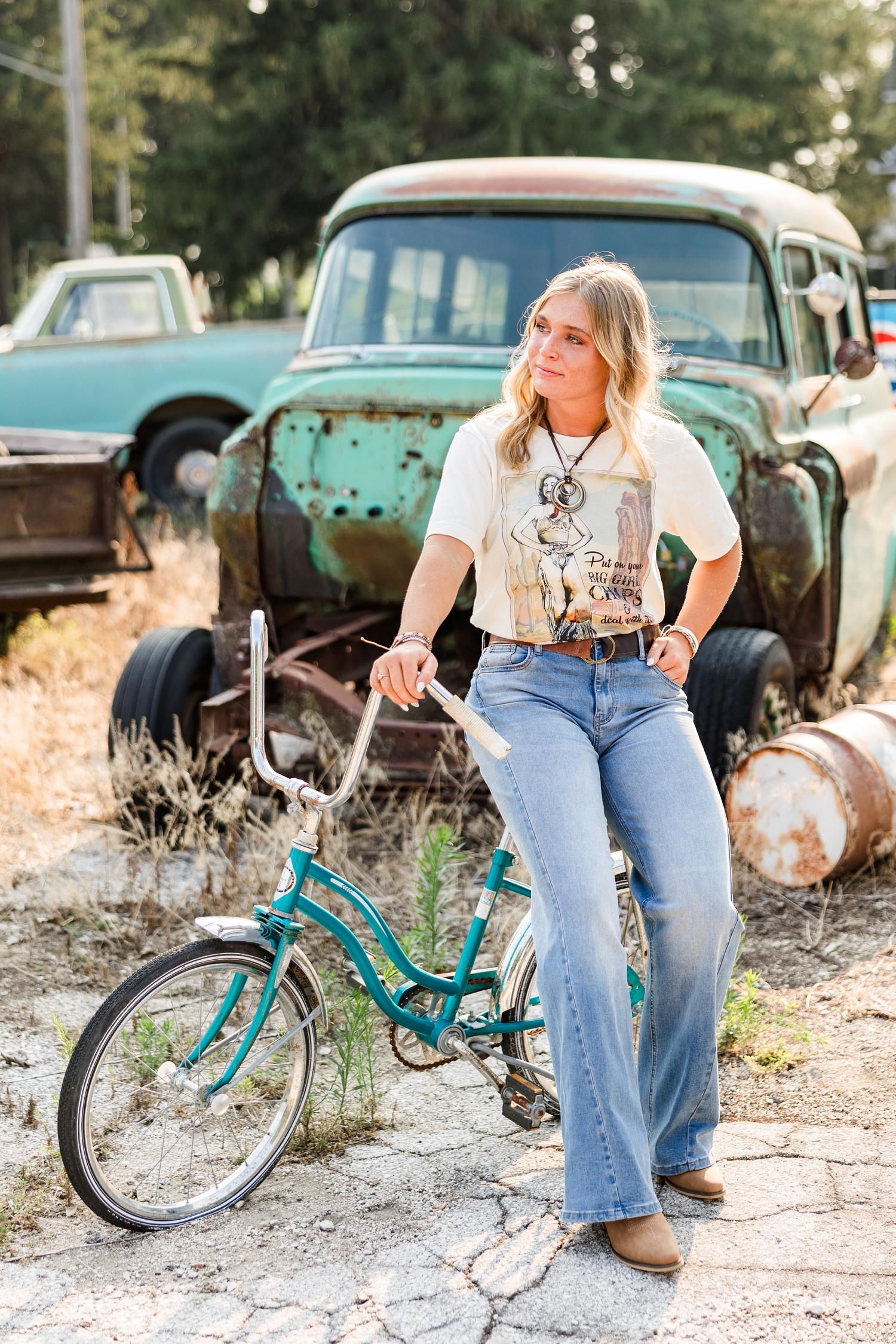 Audrey, dressed in a grunge look, side sits on an old teal bike at a broken down gas station as she looks to the left | CB Studio