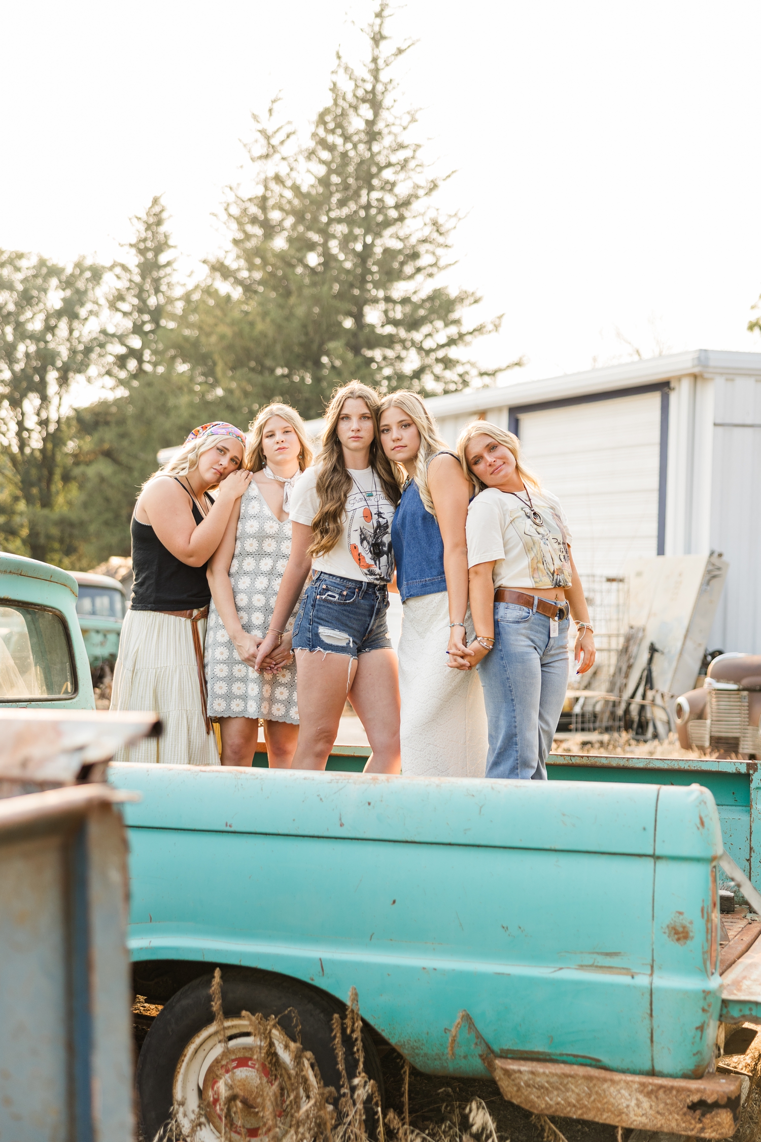 TEAM 27, dressed in boho, grunge looks, stand close holding hands in the bed of an old teal truck | CB Studio