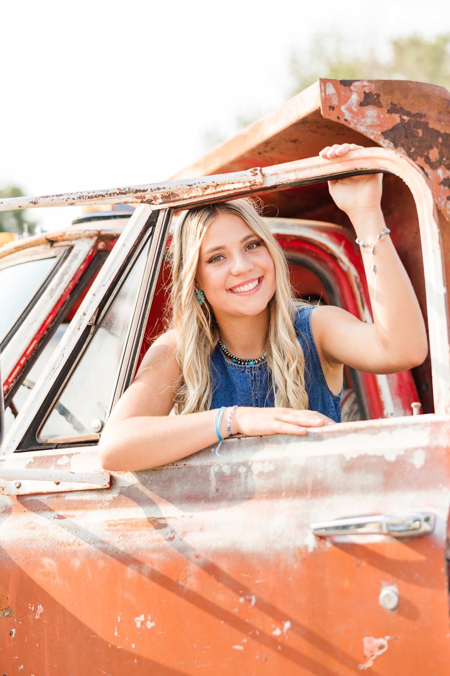 Emma, dressed in boho, grunge looks, leans out of the window of an old rustic red dump truck | CB Studio