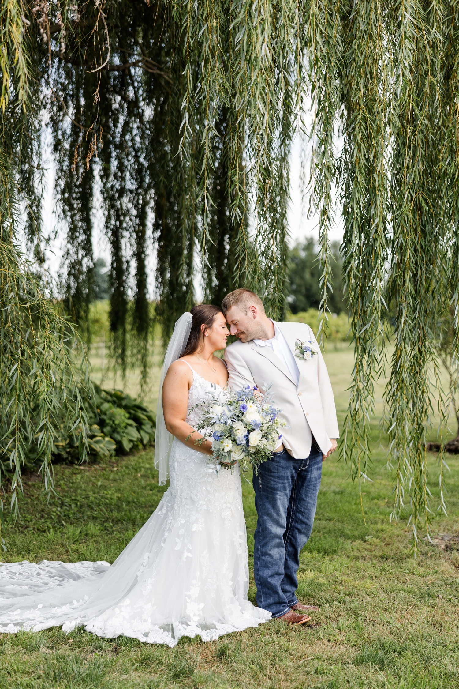 Ryan and Cassie rest their foreheads together as they stand under the tall and long branches of a weeping willow at River Valley Orchards | CB Studio