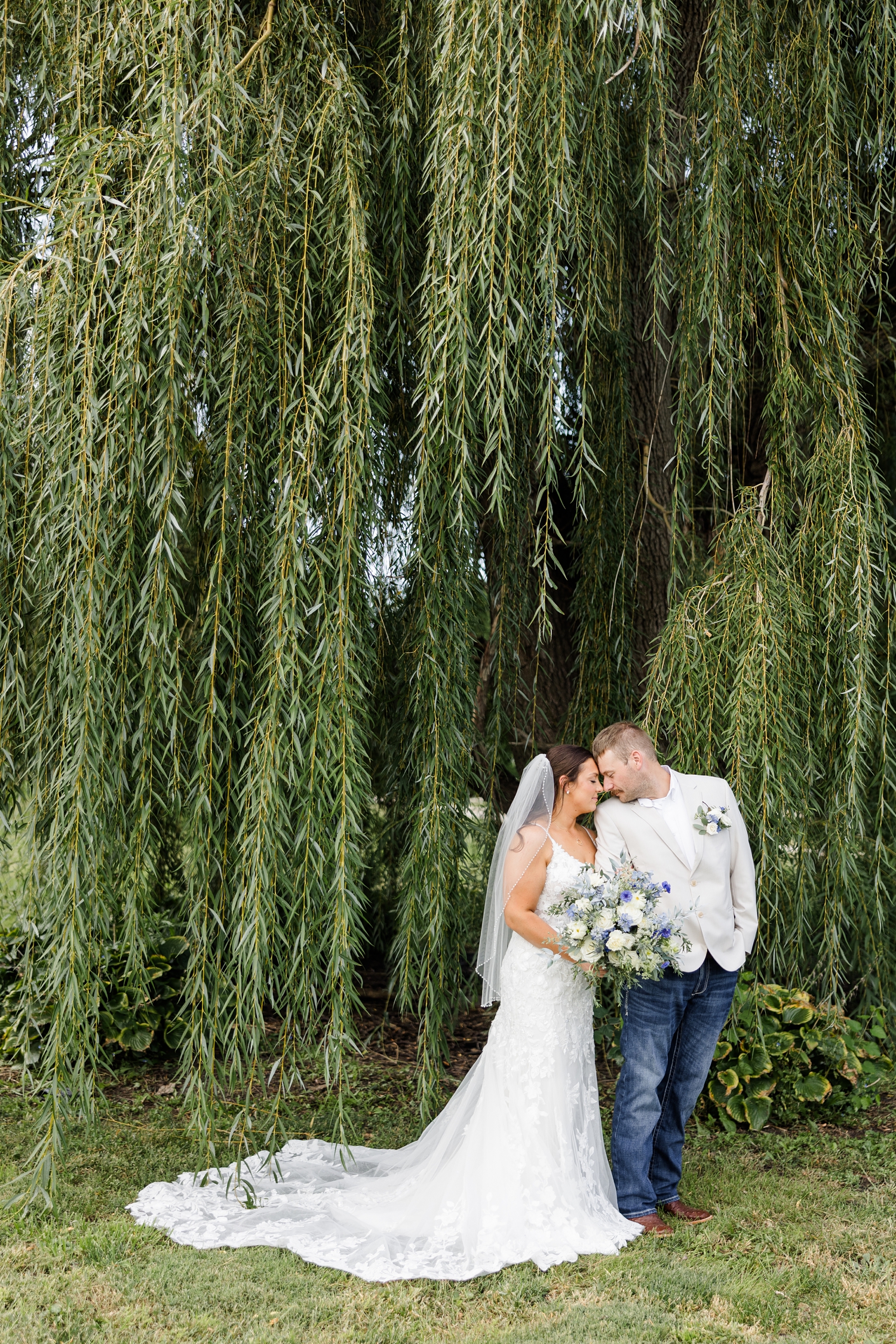 Ryan and Cassie rest their foreheads together as they stand under the tall and long branches of a weeping willow at River Valley Orchards | CB Studio